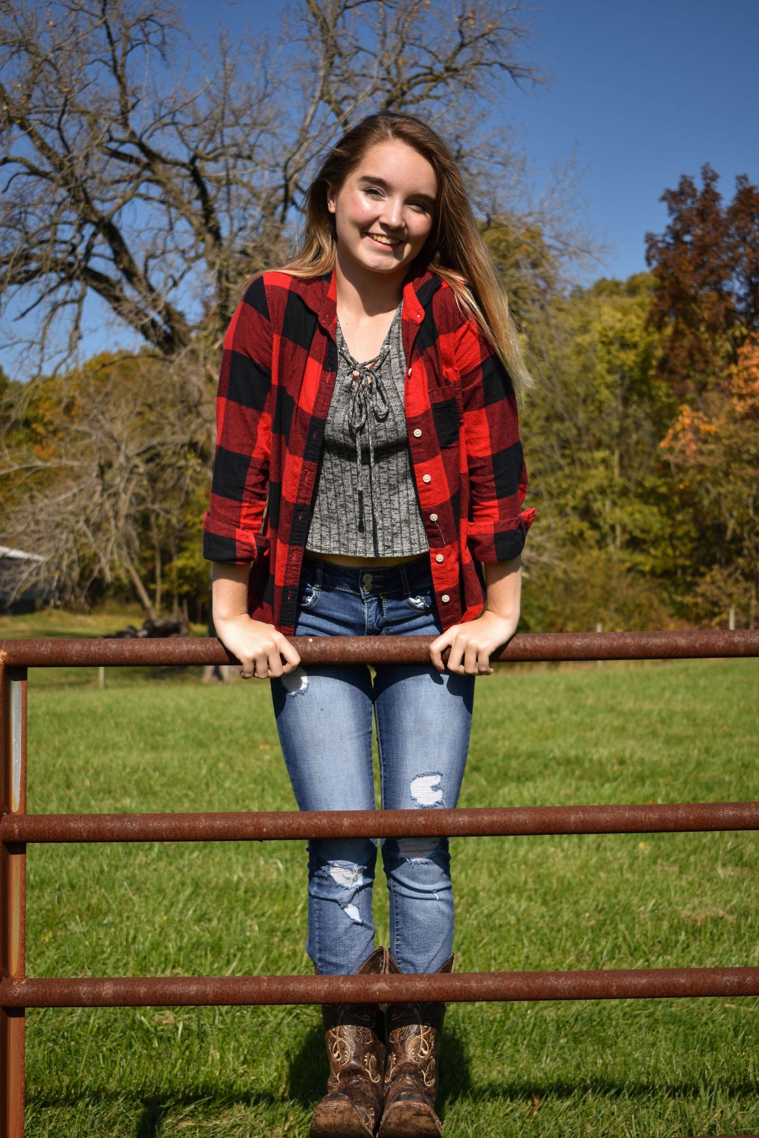 A lady is on a fence as though she is about to climb over it and is smiling.