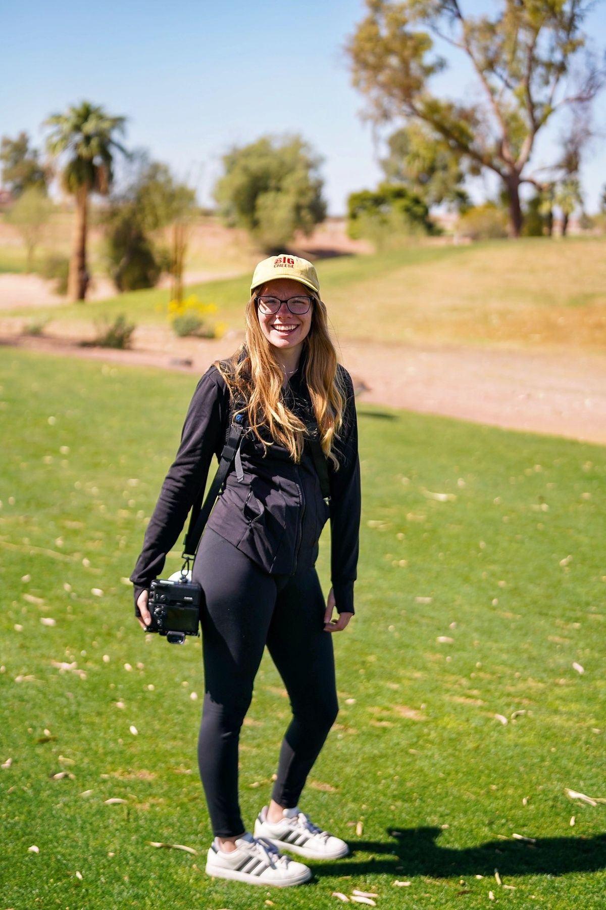 Danielle Gantt on a golf course with a camera smiling.