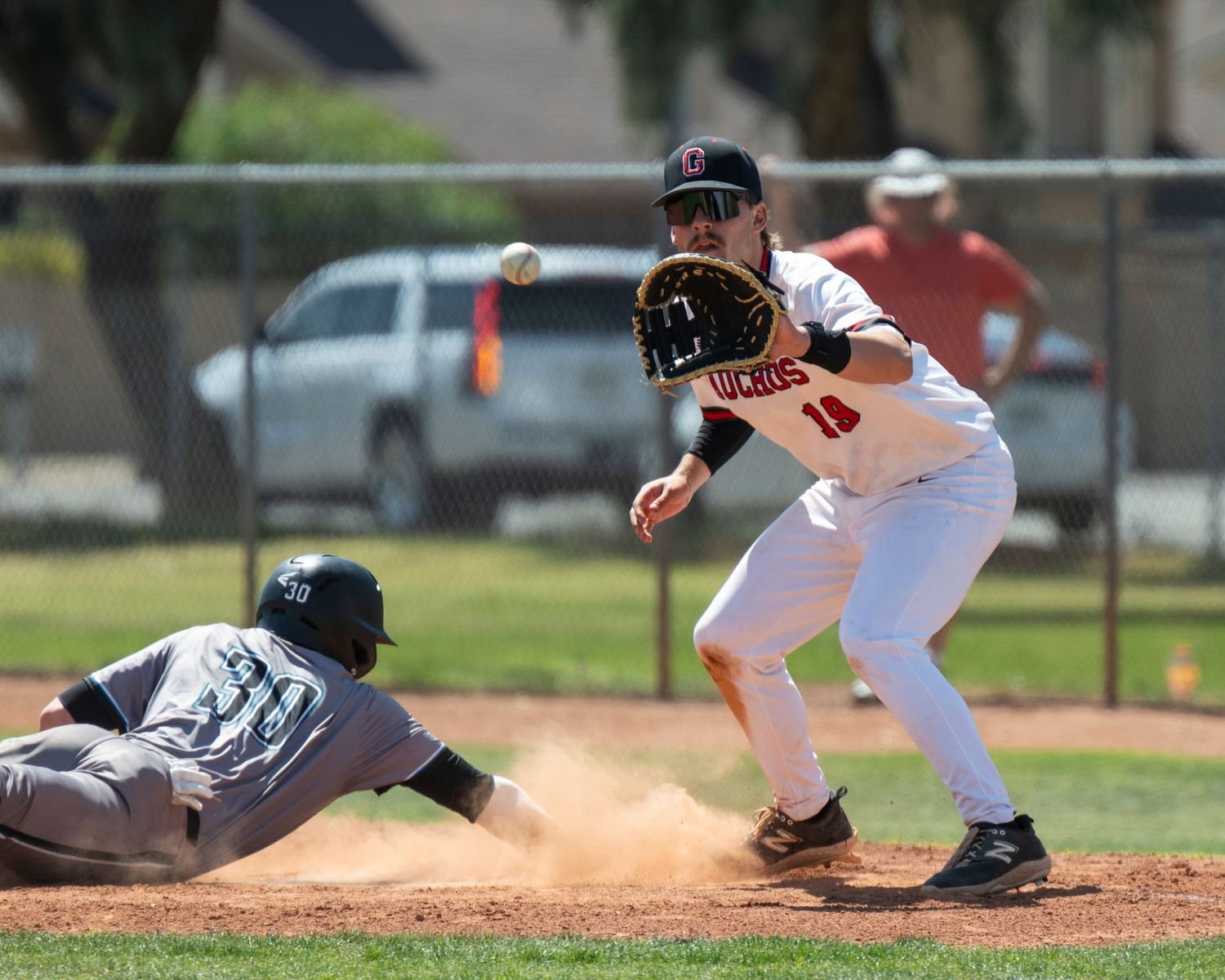 Baseball player who is about to catch a baseball and another player who took a dive to the base.