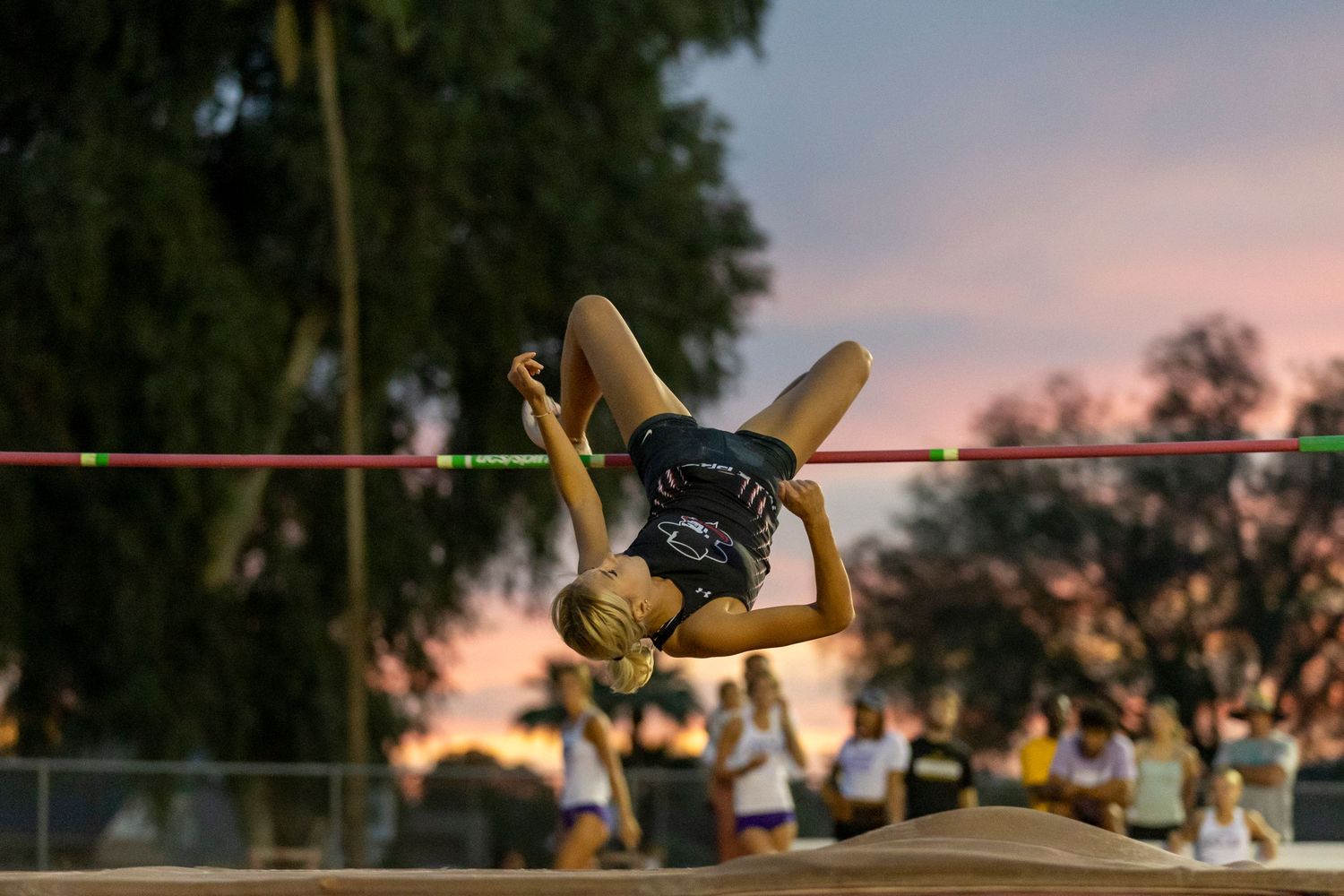 High jumper in the air and coming over the pole after already jumping.