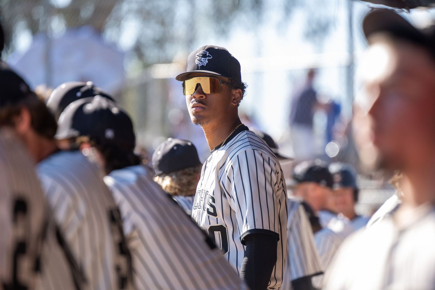 Baseball player standing in dugout surrounded by his teamates.