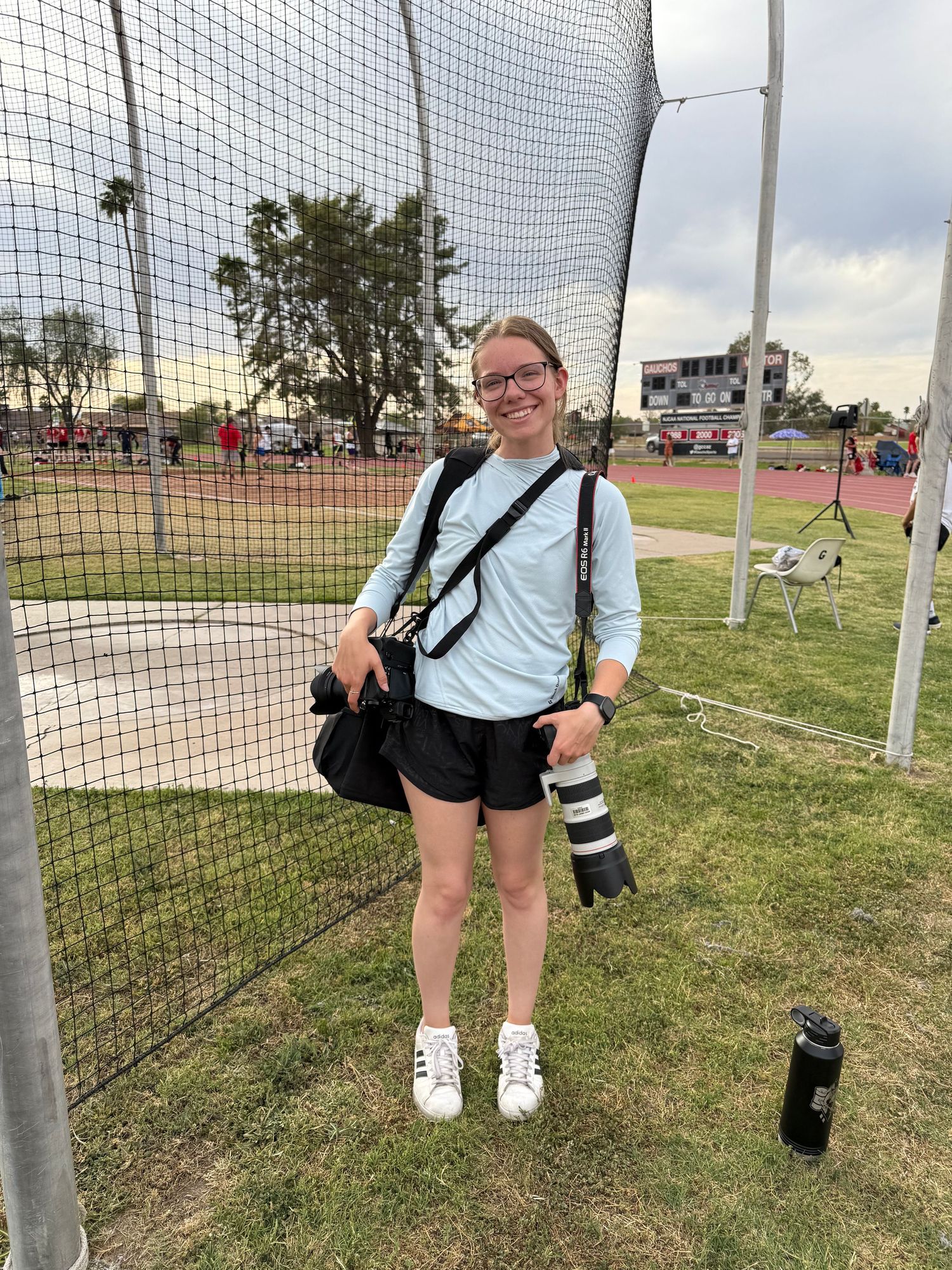 Danielle Gantt at a track and field meet holding two cameras and smiling.
