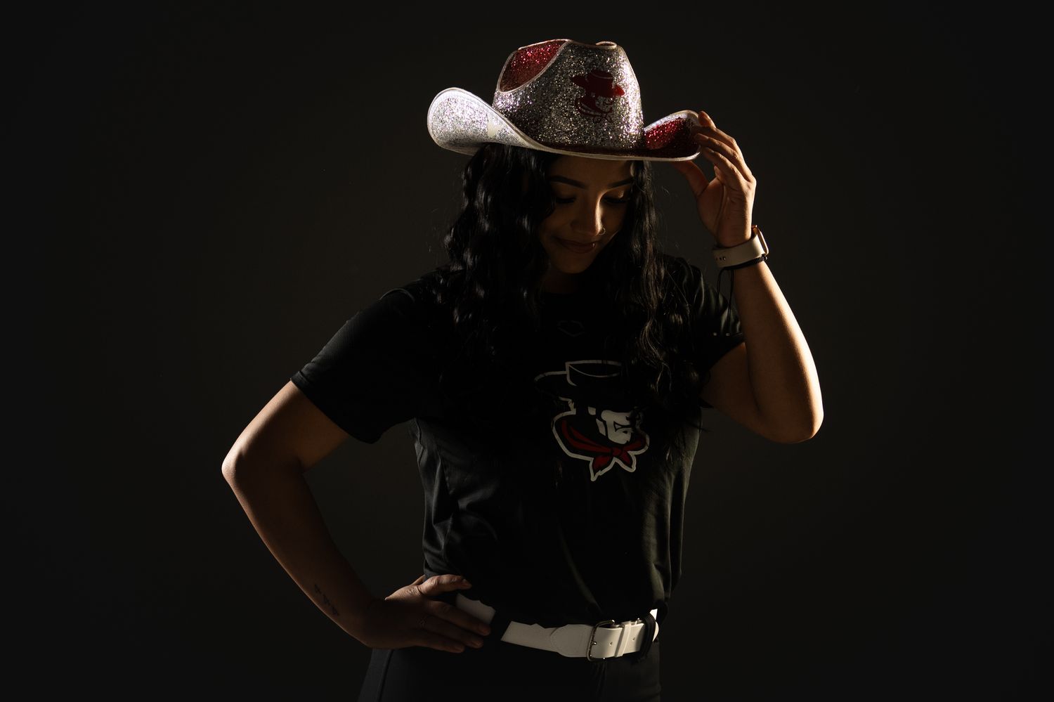 Softball player posing in a moody photo with a cowboy hat.