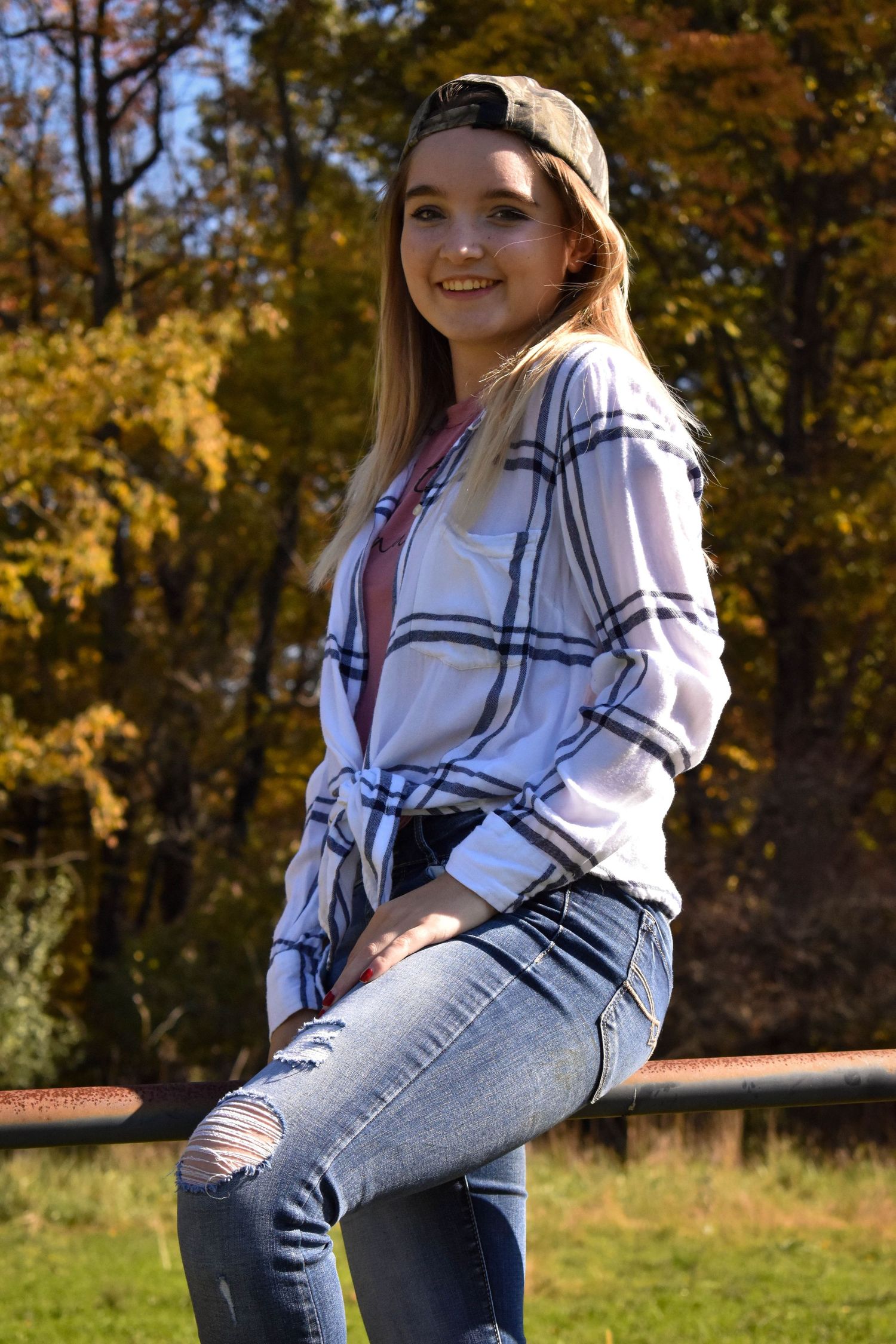A lady is sitting on a fence, one leg on each side and is smiling.