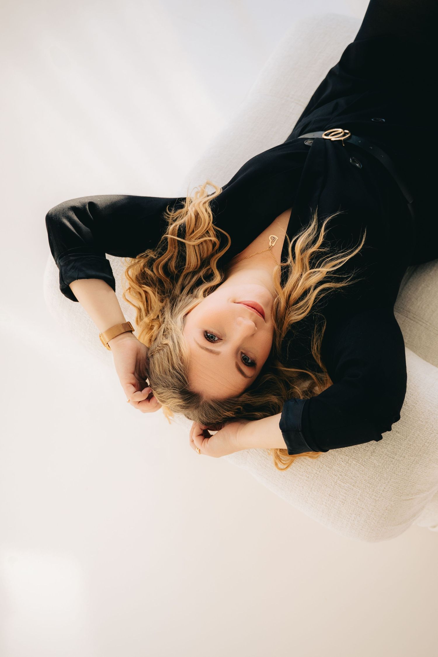 Overhead view of a blonde woman in black outfit lying on a white floor looking up.