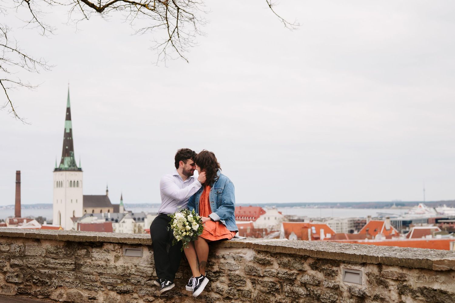 Couple sharing a kiss on a stone wall overlooking the historic rooftops of Tallinn, Estonia.