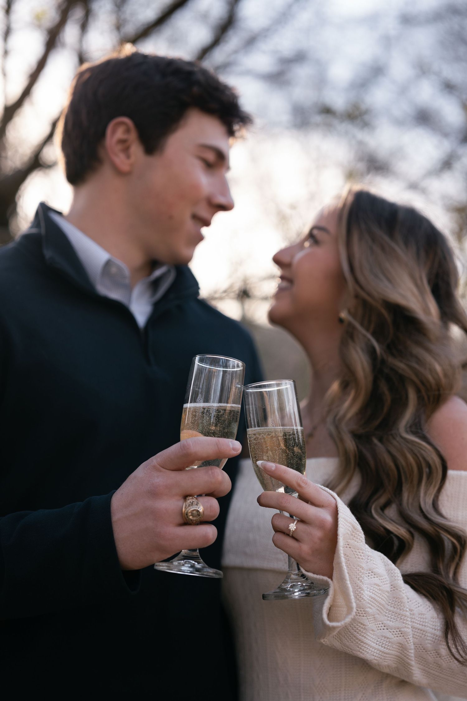 Romantic couple shares champagne toast while gazing at each other in outdoor winter setting.