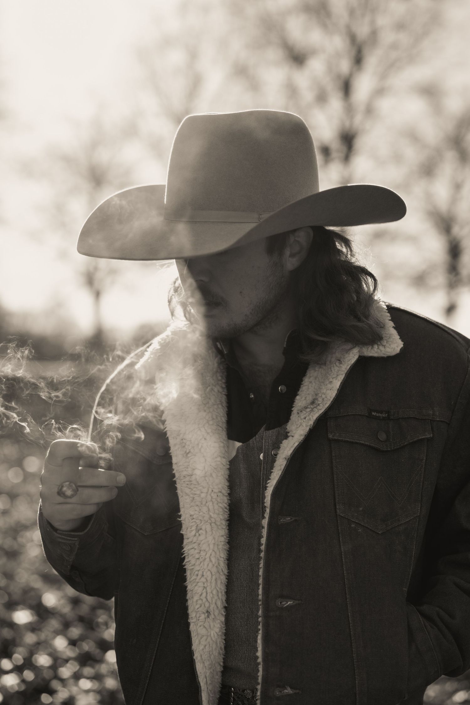 Atmospheric black and white portrait of cowboy smoking in sheepskin jacket.