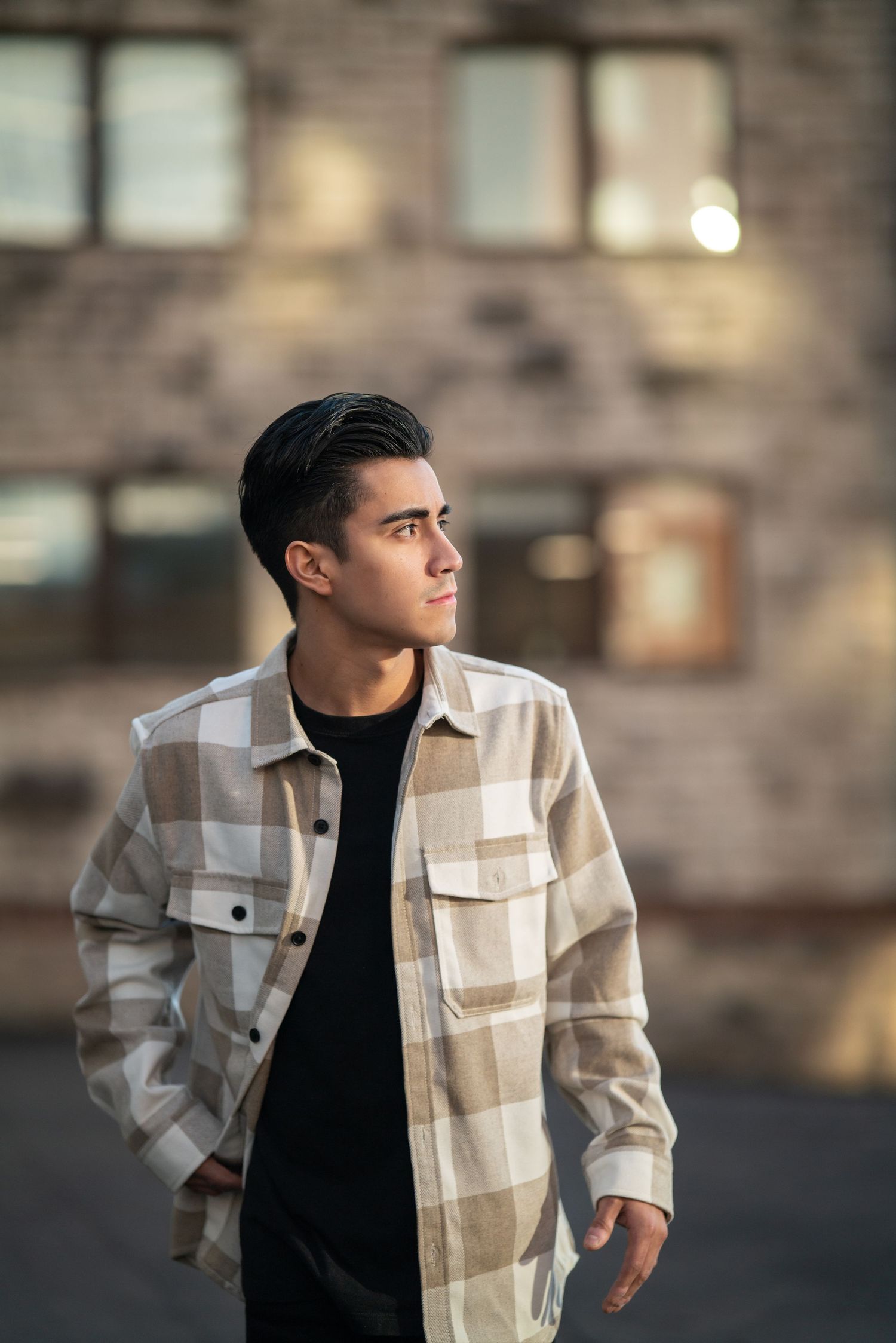 Young person wearing a checkered jacket and black shirt against an urban backdrop.