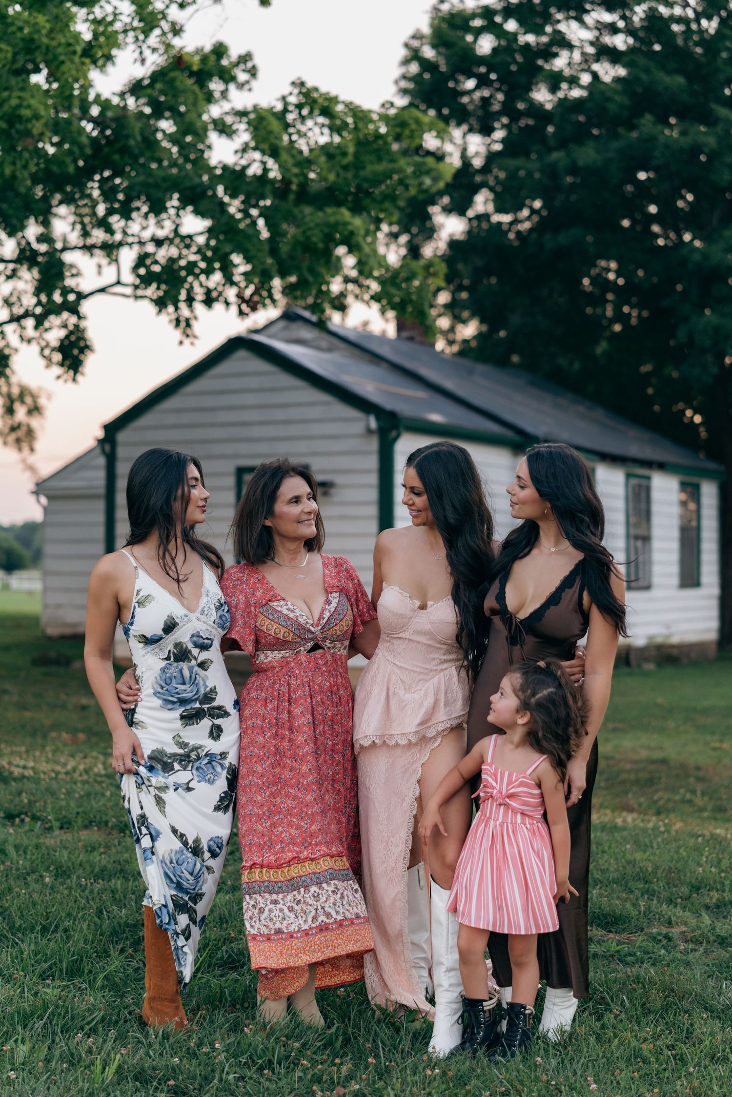 Group of women and child in stylish dresses pose together outdoors.