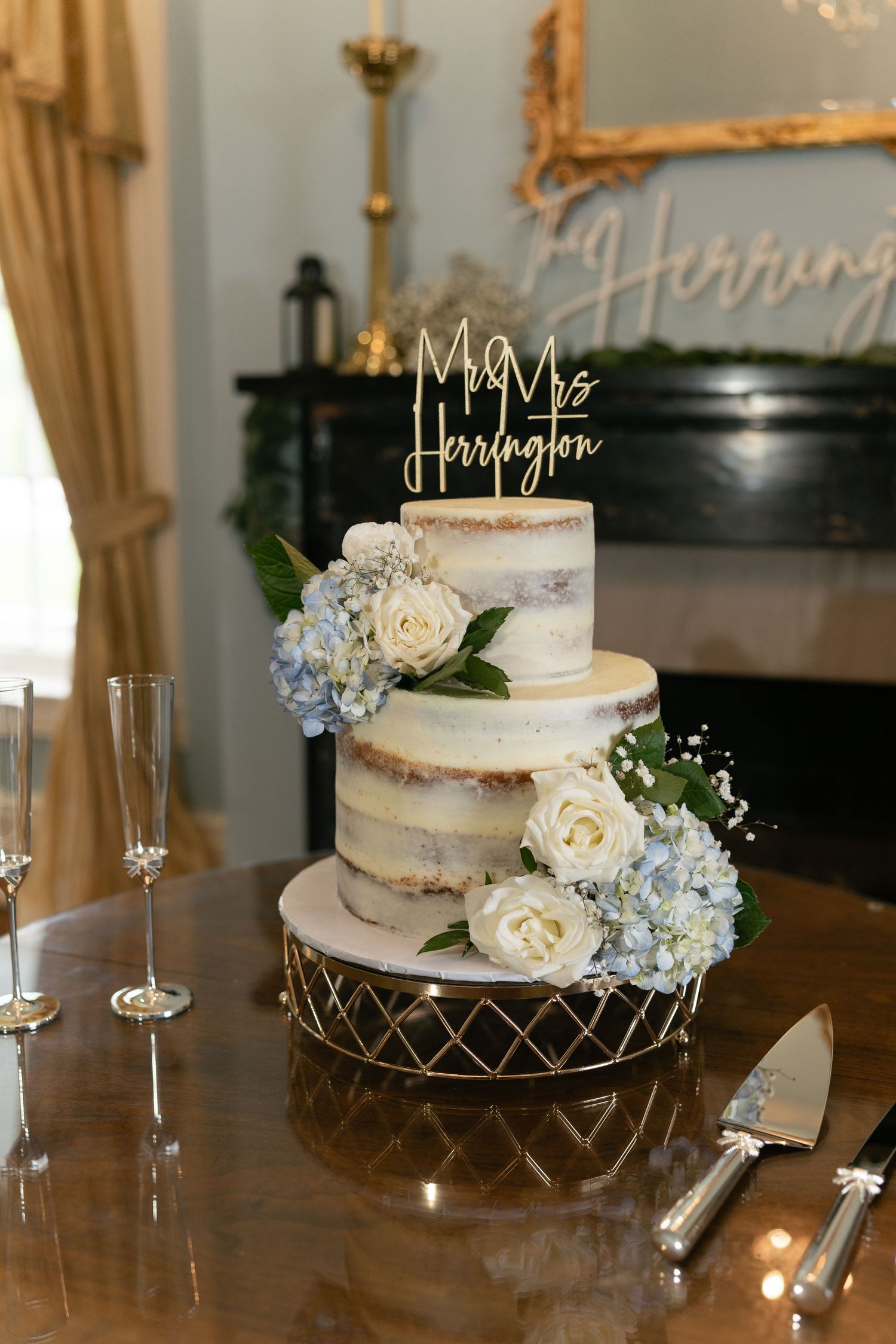 Elegant three-tier semi-naked wedding cake decorated with white roses and blue hydrangeas.