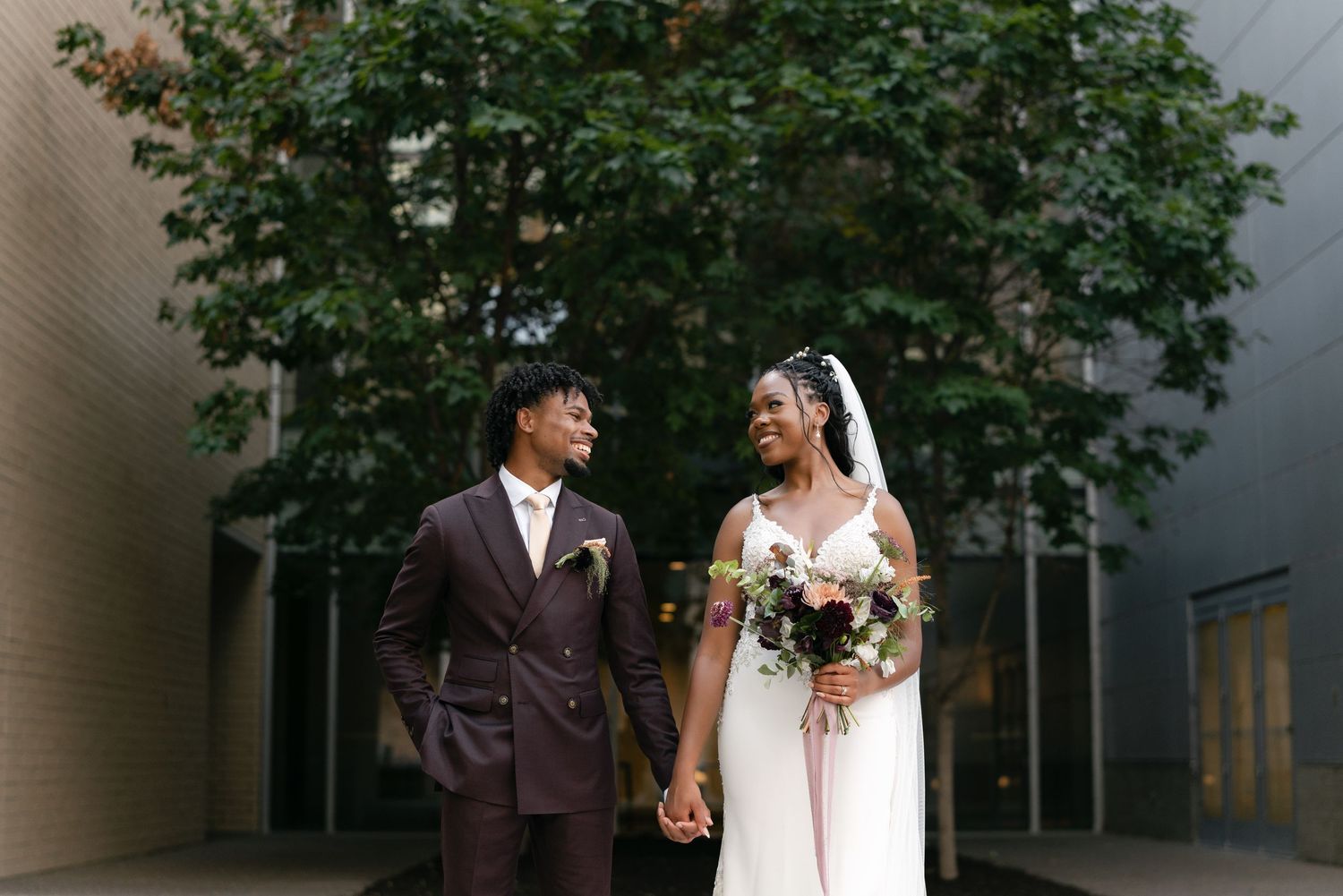 A couple in wedding attire holding hands while walking together through an urban setting.