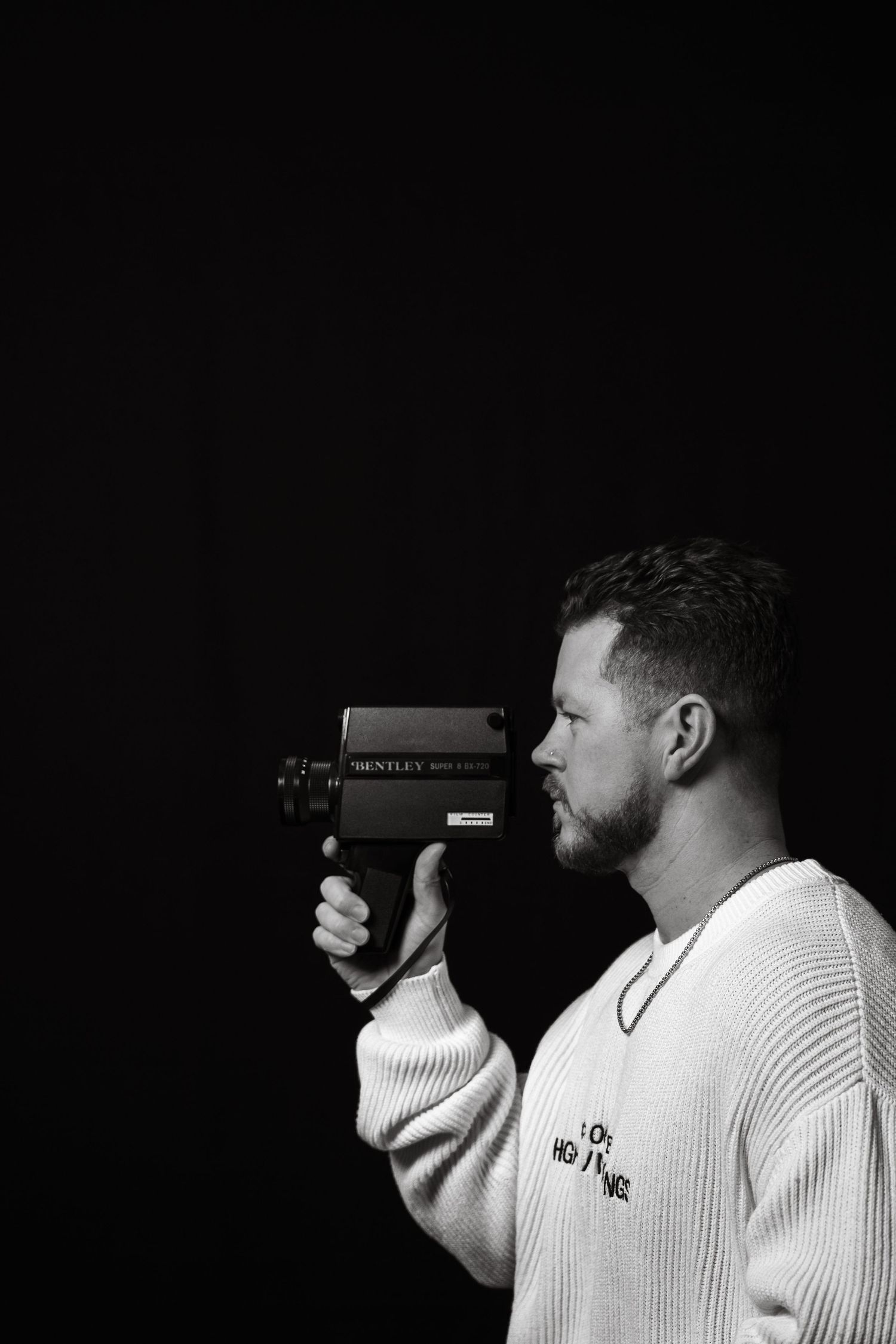 Dramatic side view of person holding vintage camera while wearing white knit sweater.