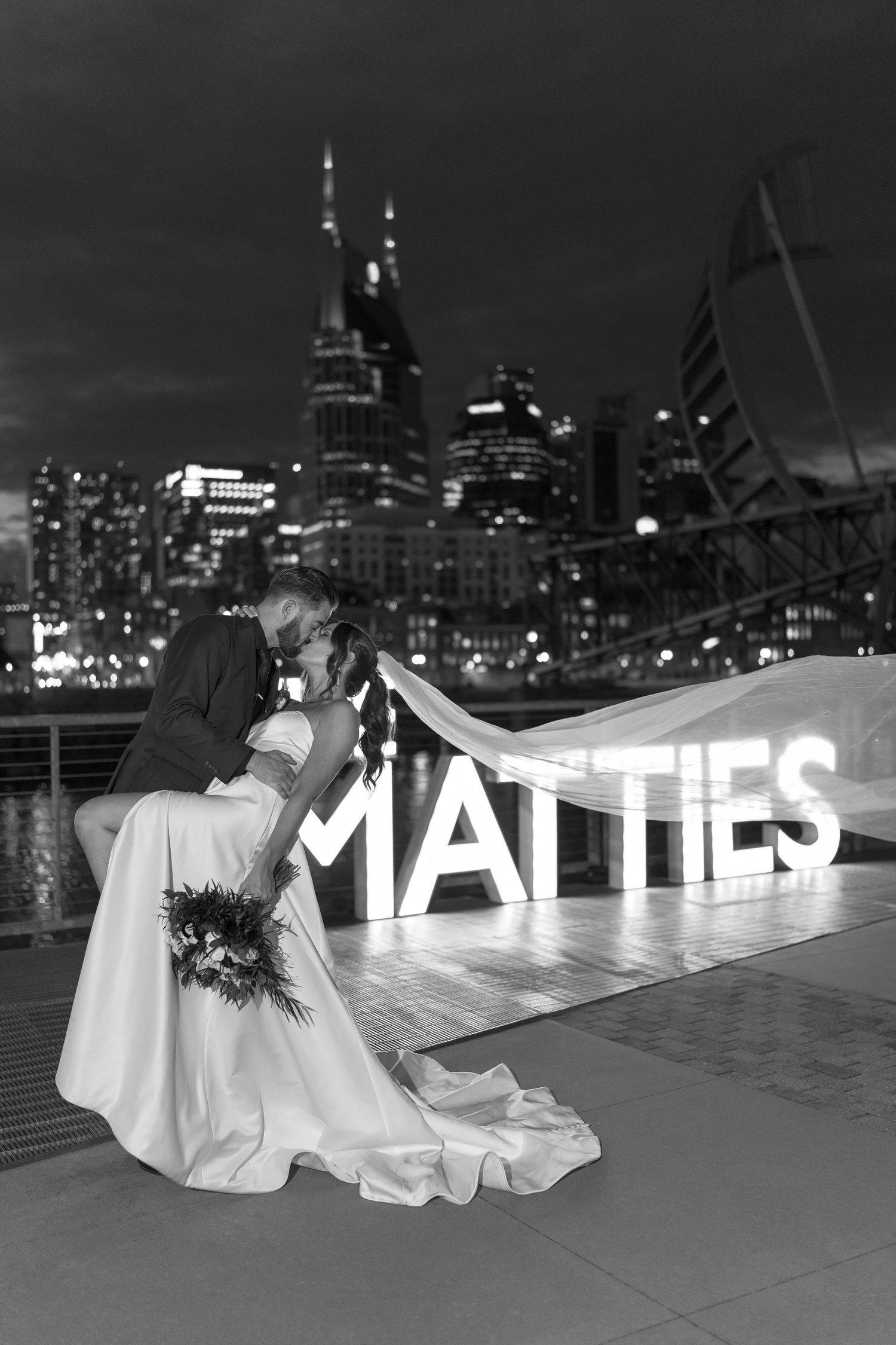 Black and white wedding photo with city skyline and illuminated MATTIES sign.