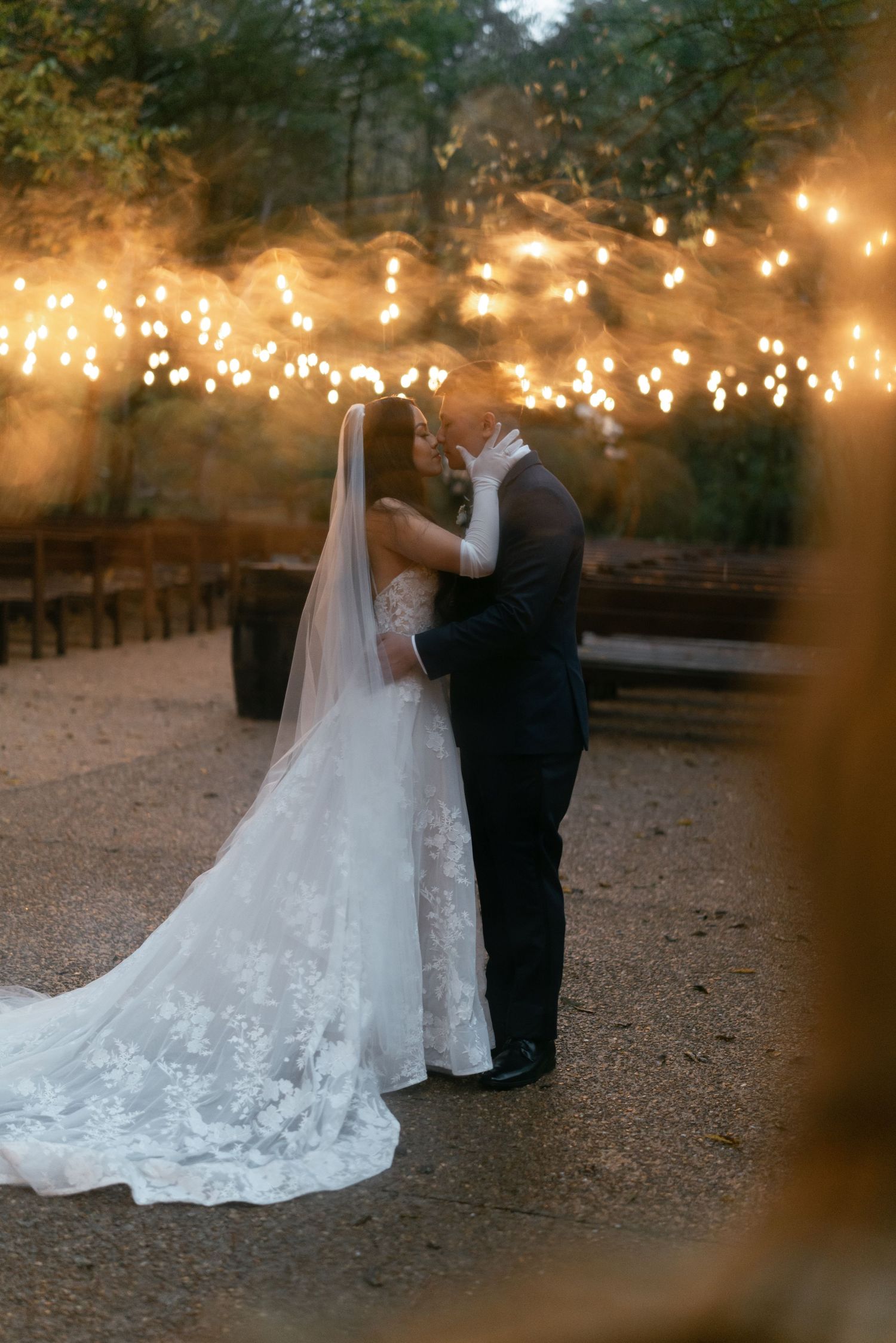 A romantic outdoor wedding scene illuminated by string lights at dusk with a lace wedding gown.