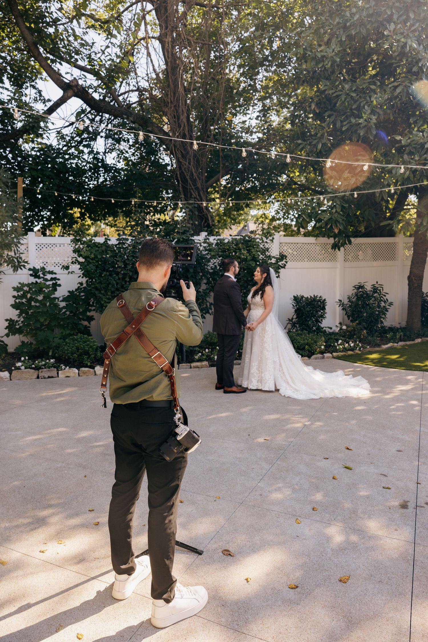 Wedding photographer capturing bride and groom portraits outdoors in a garden setting with string lights.