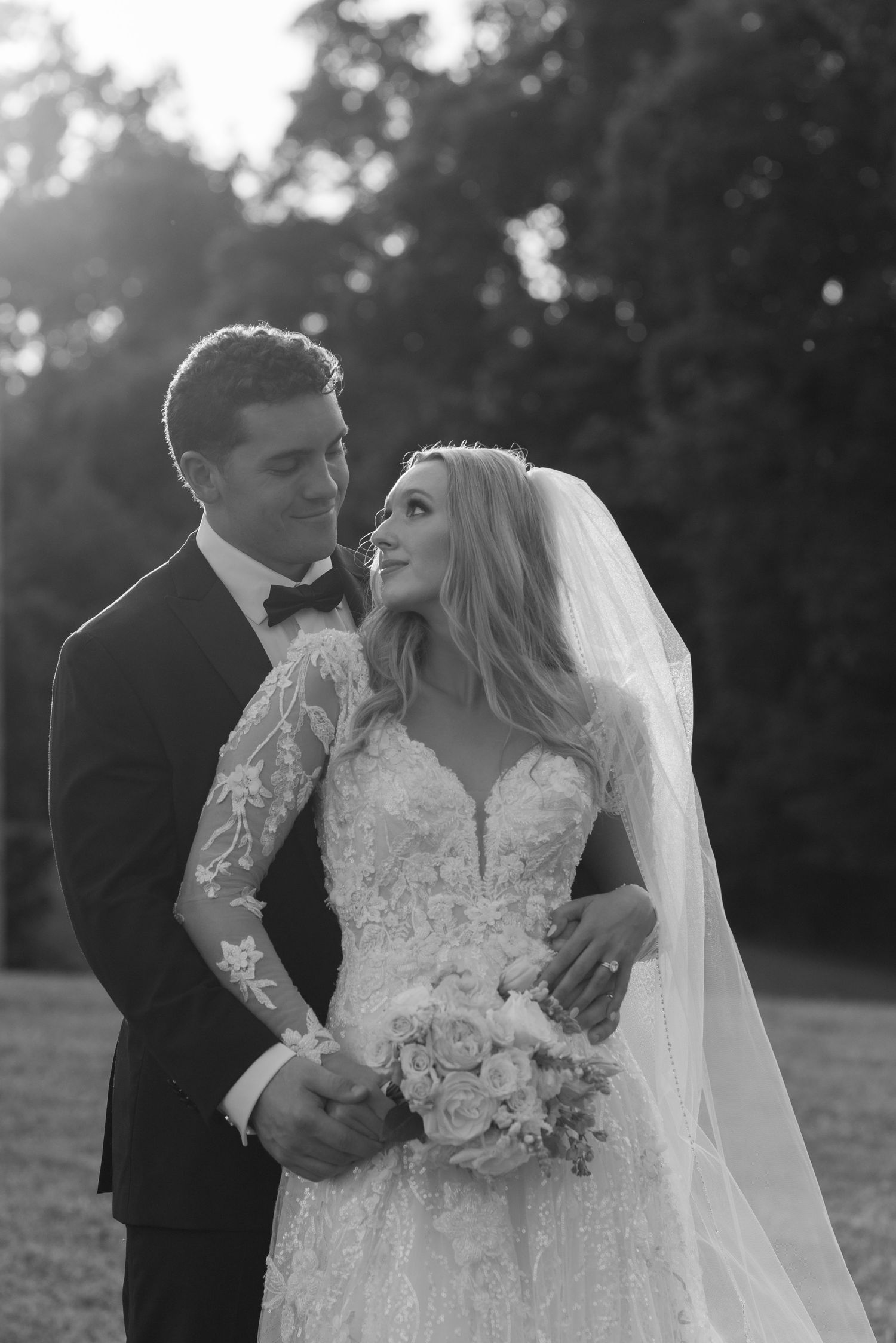 Romantic black and white wedding portrait captured at sunset in garden setting.