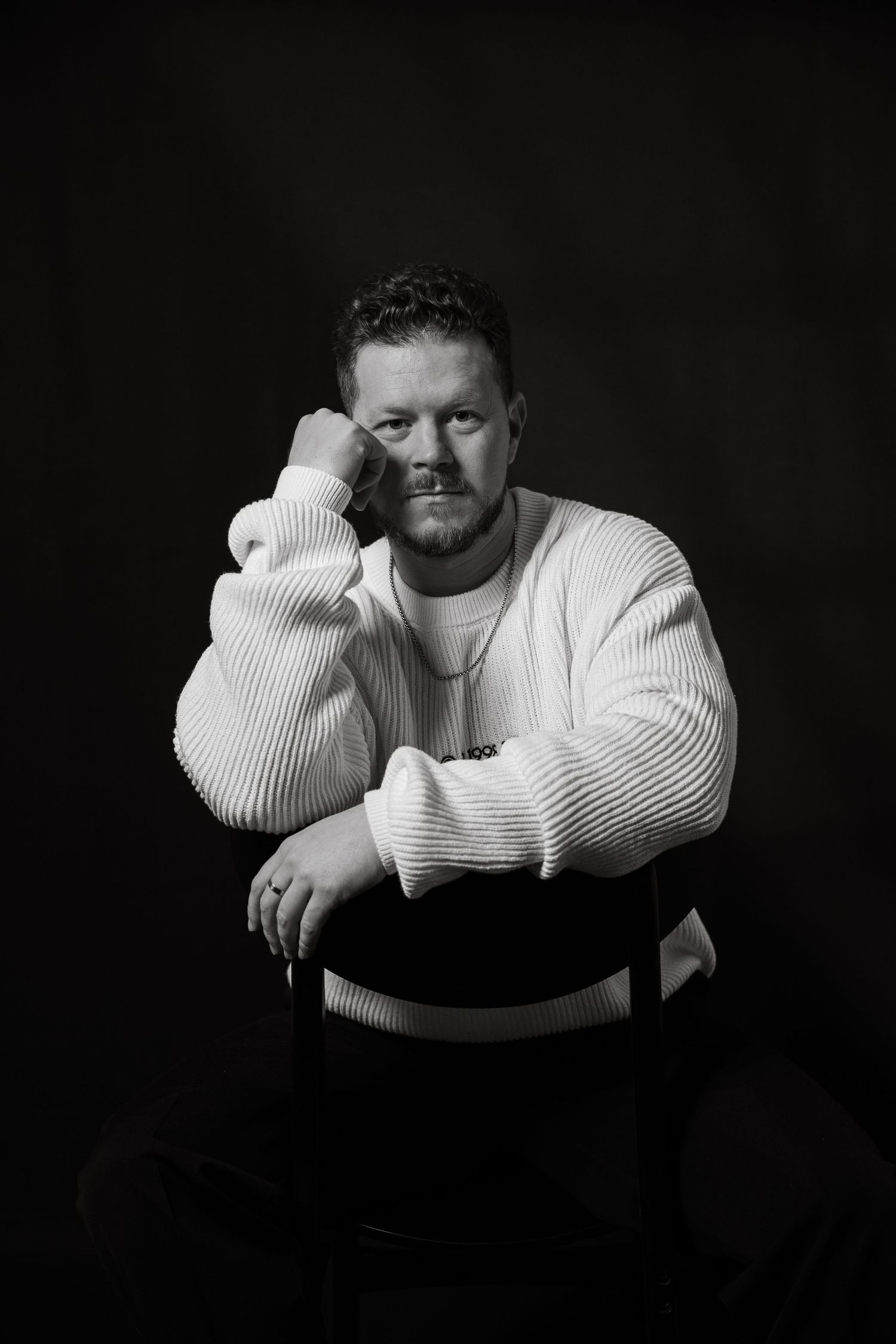 Moody black and white studio portrait of person in white sweater with contemplative pose.