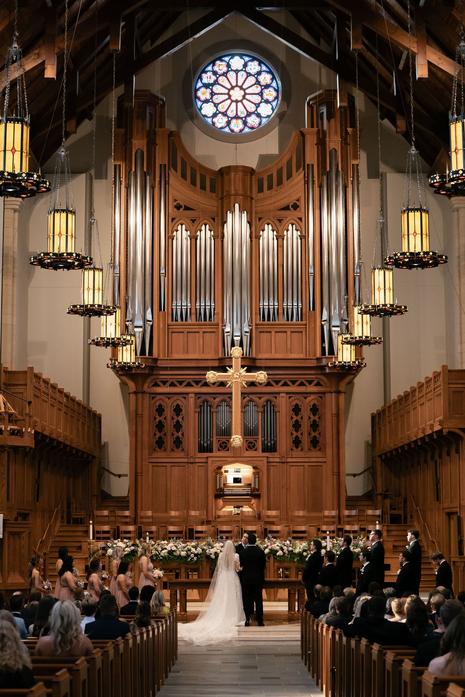 A traditional church wedding ceremony takes place beneath towering organ pipes and a beautiful rose window.