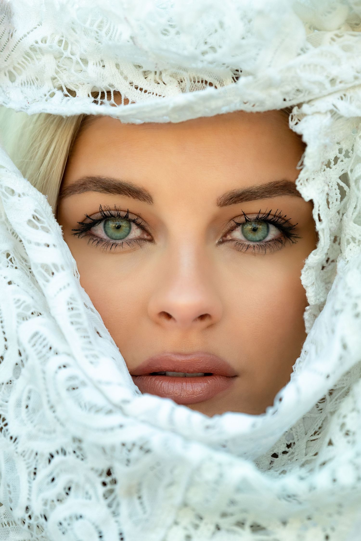 Close-up portrait framed by white lace showing striking green eyes and natural makeup.