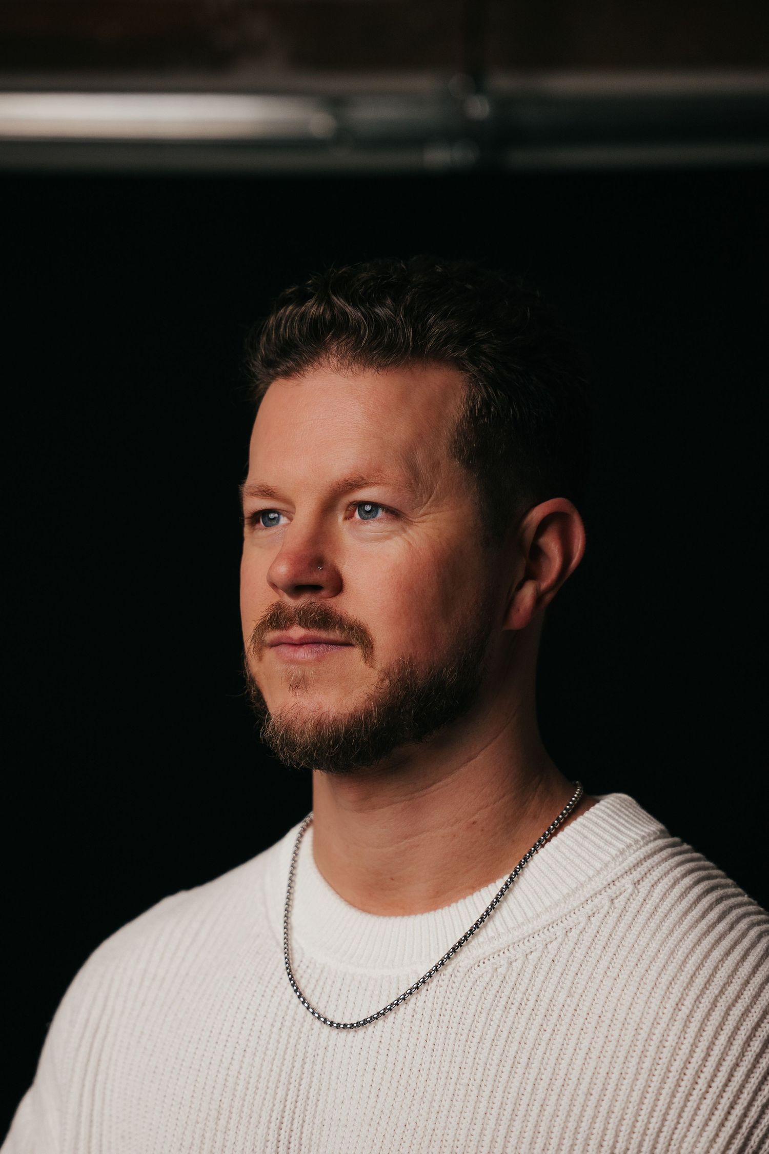 Portrait against dark background of person in white t-shirt wearing silver chain necklace.