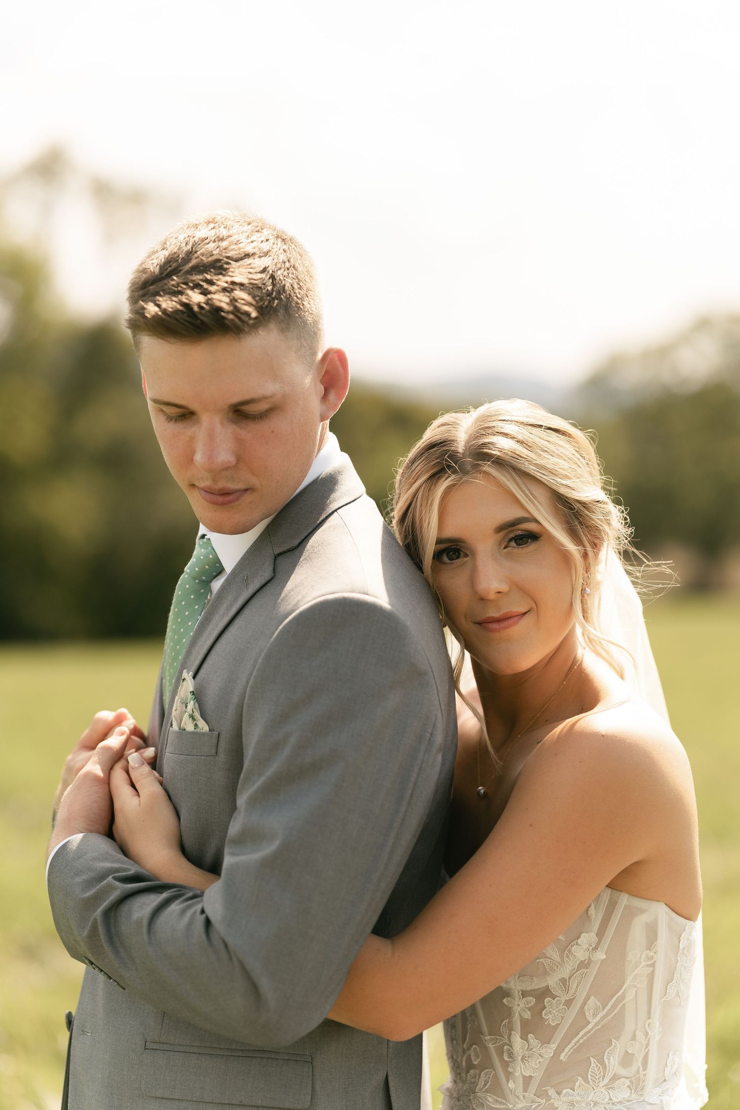 A romantic wedding photo featuring a couple in gray suit and strapless white dress embracing outdoors.