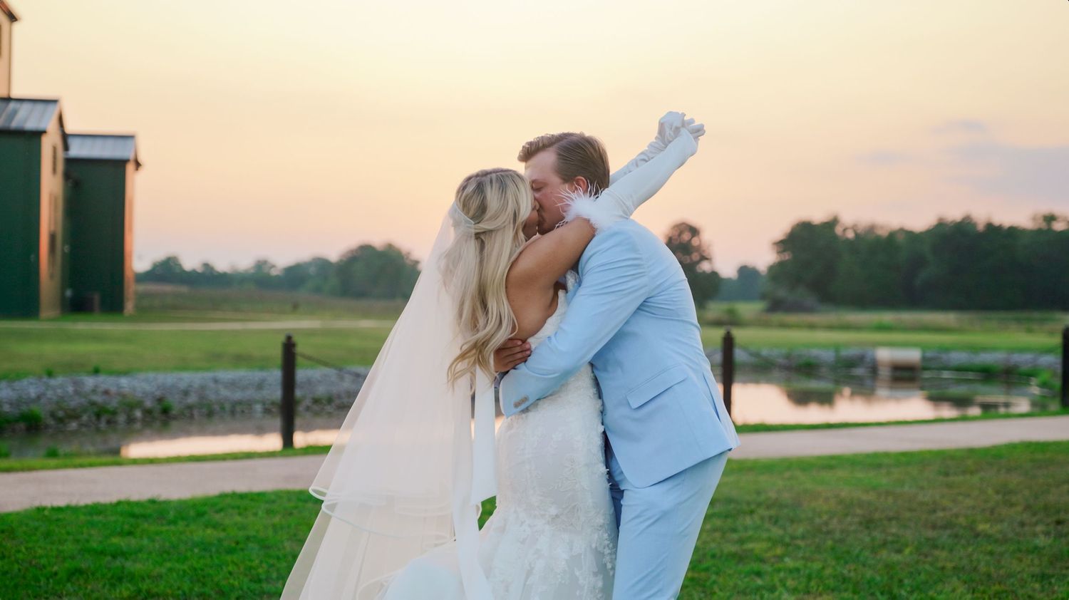 Romantic couple embraces at sunset in a picturesque outdoor setting with lake and greenery in background.