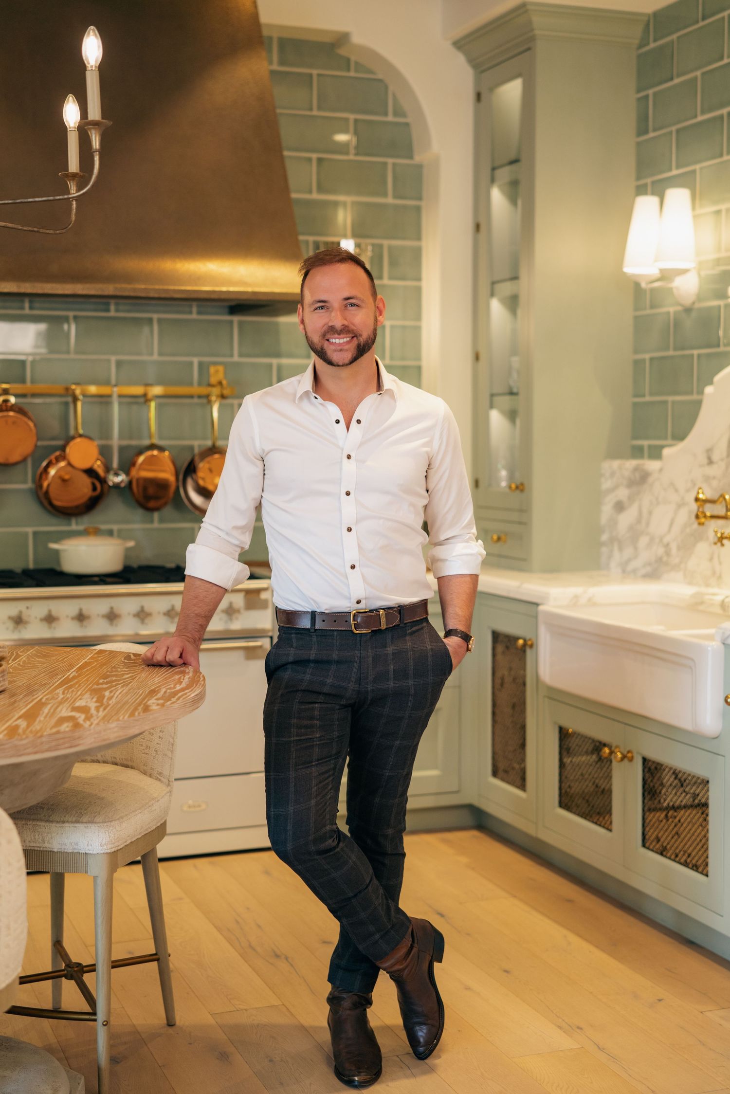 Man in white shirt and plaid pants standing in luxury kitchen interior.