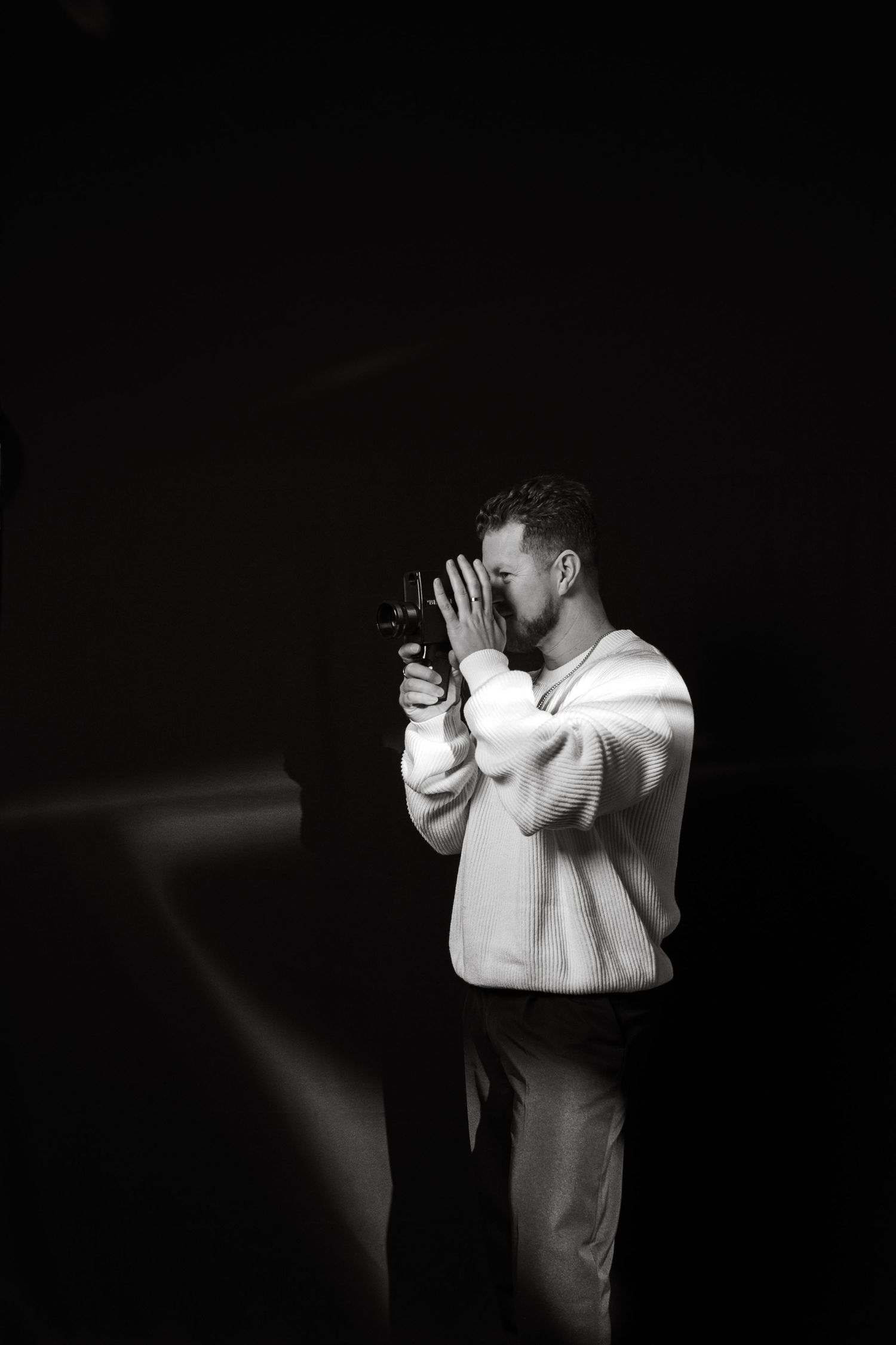 Black and white photo of videographer using vintage camera in studio setting.