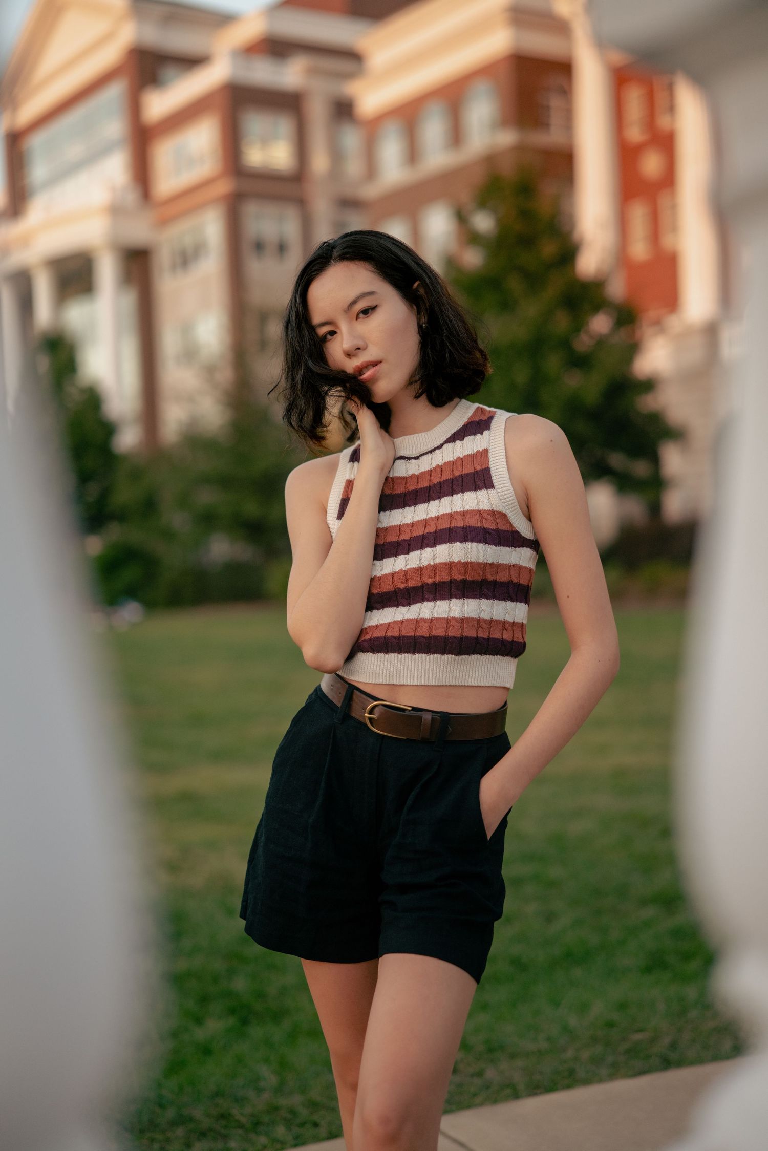 Woman in striped crop top and shorts poses casually by residential building.