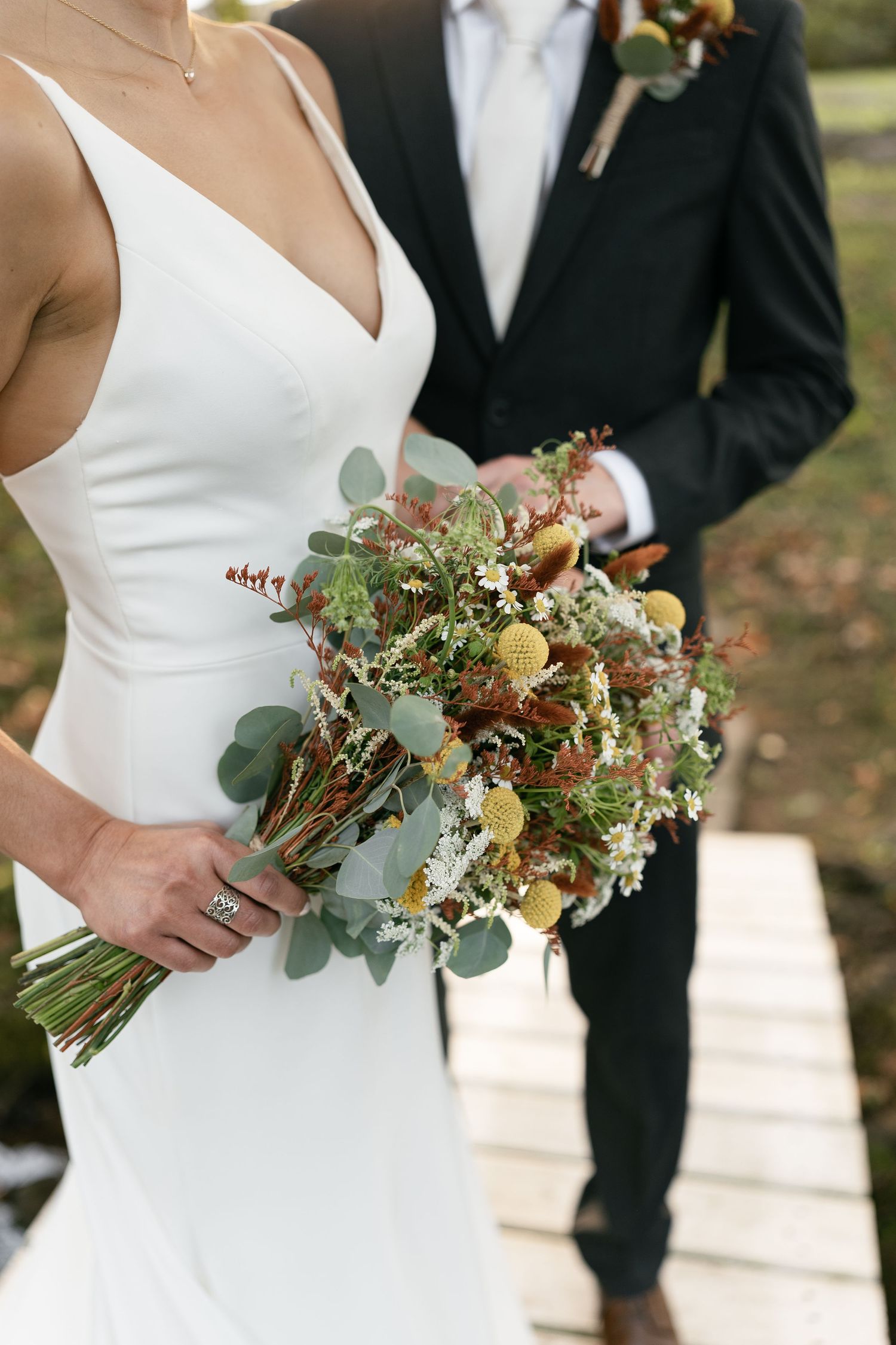 Elegant wedding bouquet with dried flowers and eucalyptus held against white bridal gown.