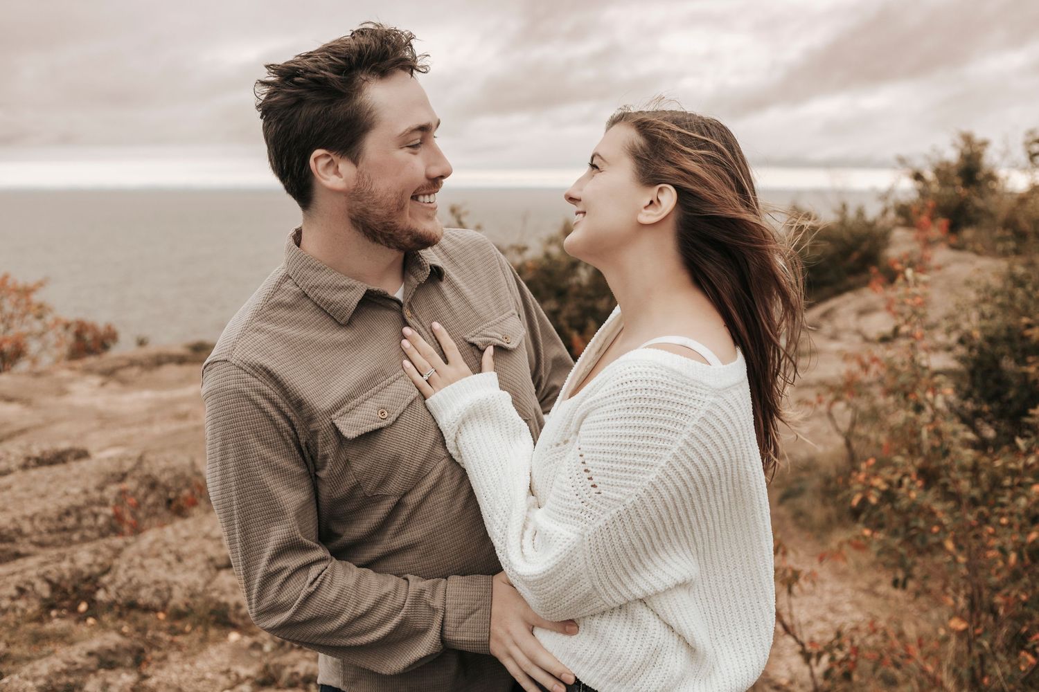 A couple shares a romantic moment outdoors in a rustic autumn landscape wearing cozy sweaters.