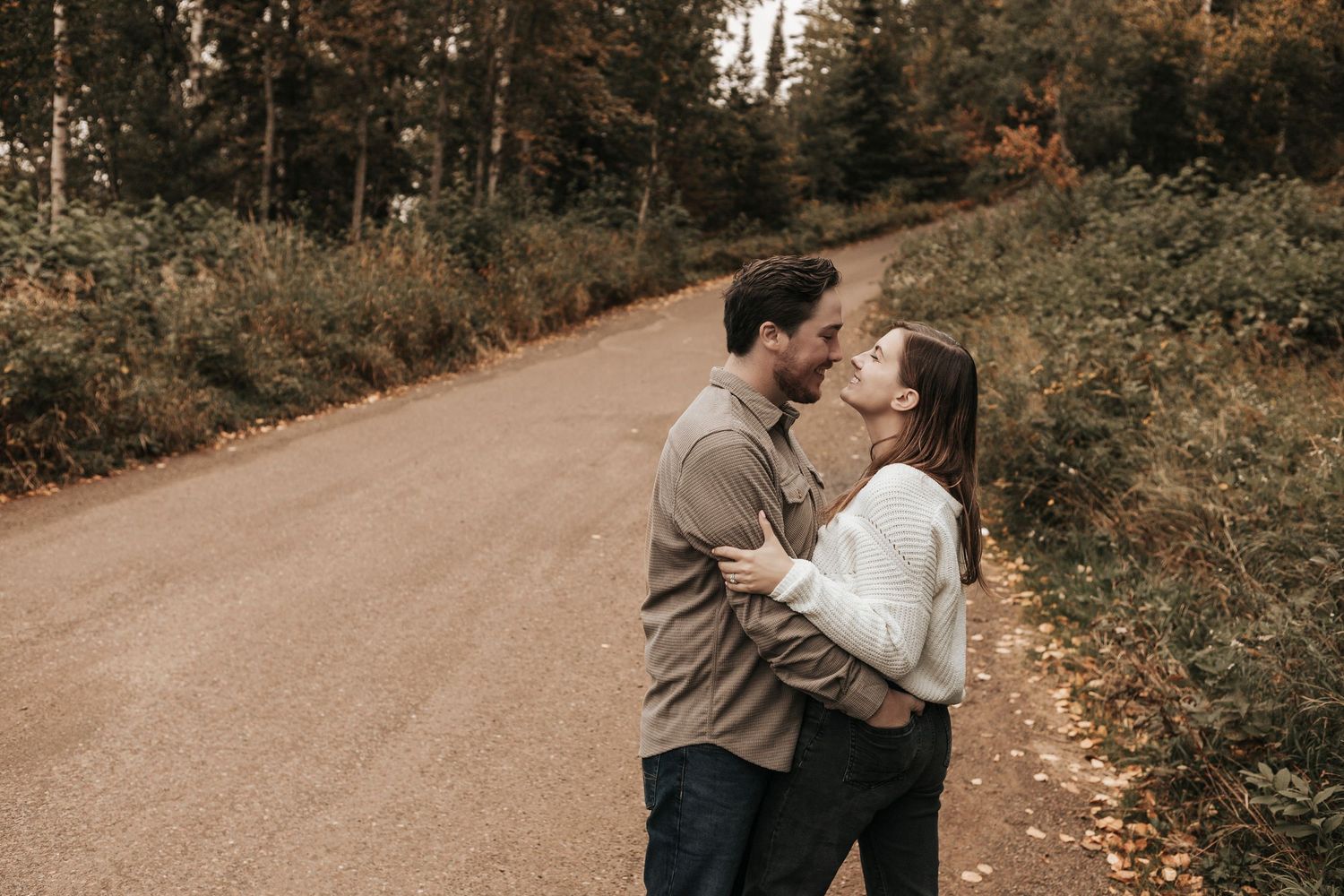 A couple shares a romantic moment on a forest path surrounded by autumn foliage and golden sunlight.