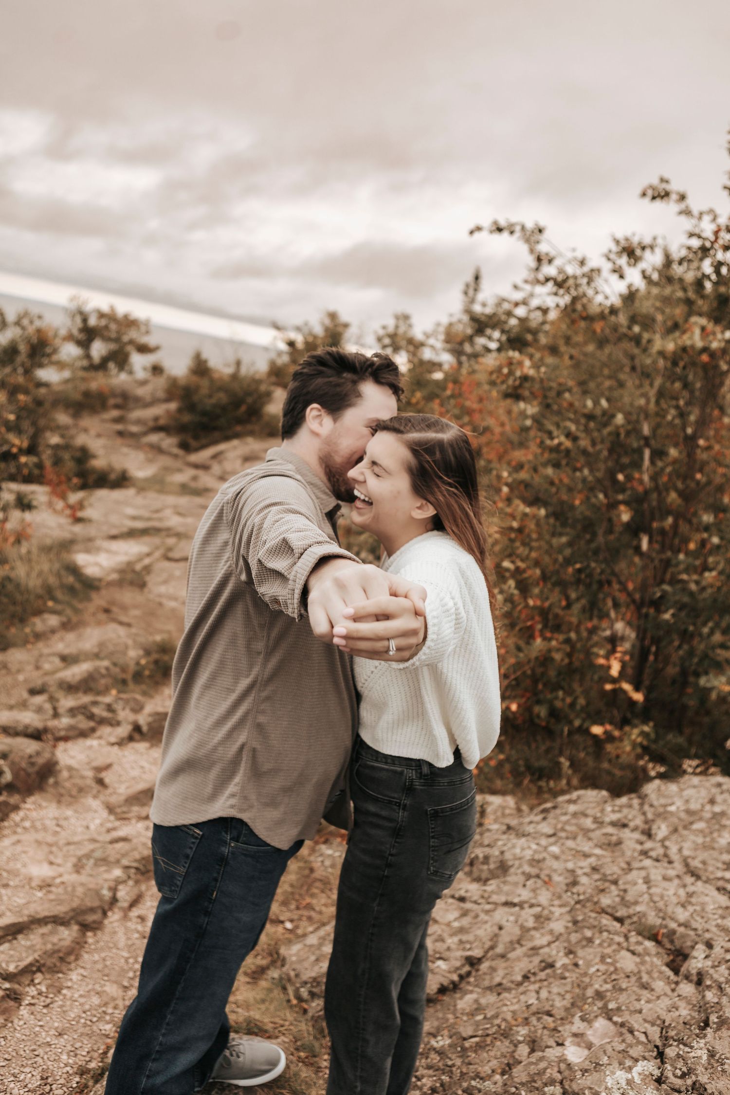 A couple shares joyful laughter together during a desert photoshoot with warm sepia tones and desert plants.