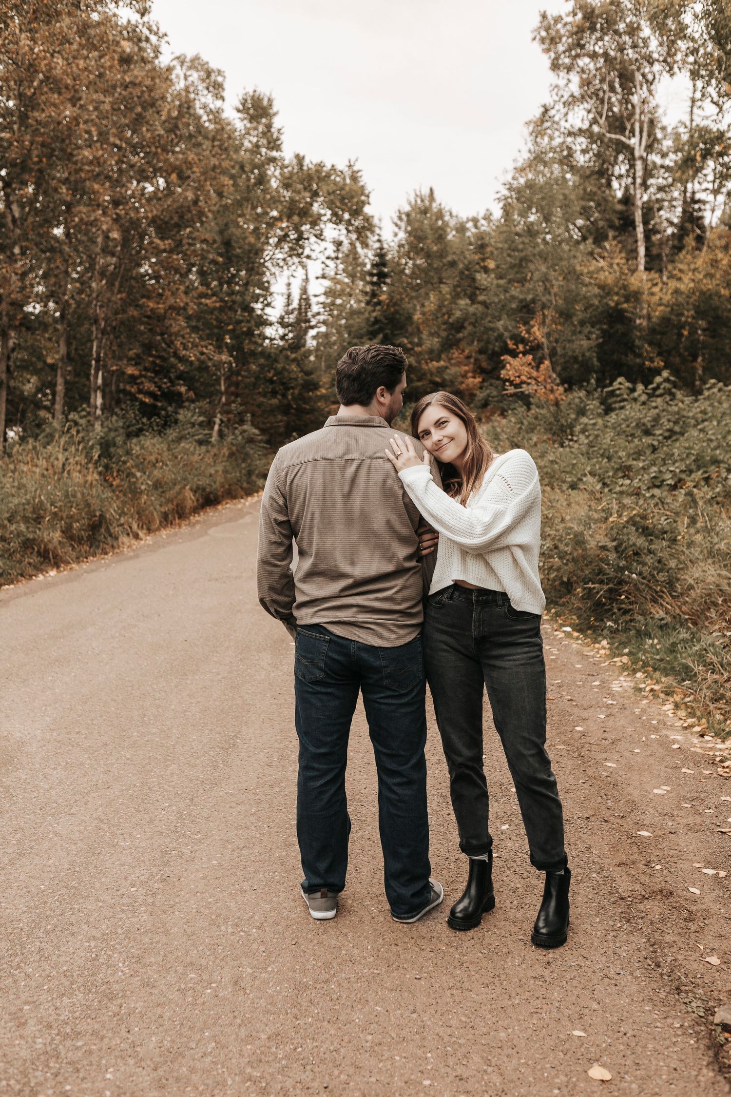 A couple walking together on a winding autumn path through trees and fallen leaves in sepia tones.