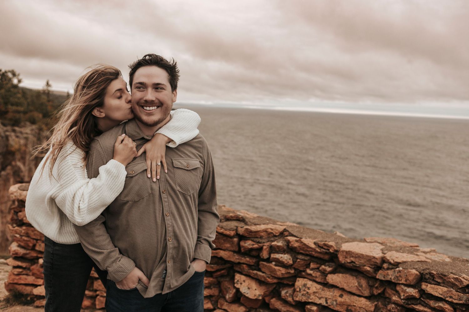 A couple shares tender moments on a rocky coastal cliff during sunset with ocean views in the background.