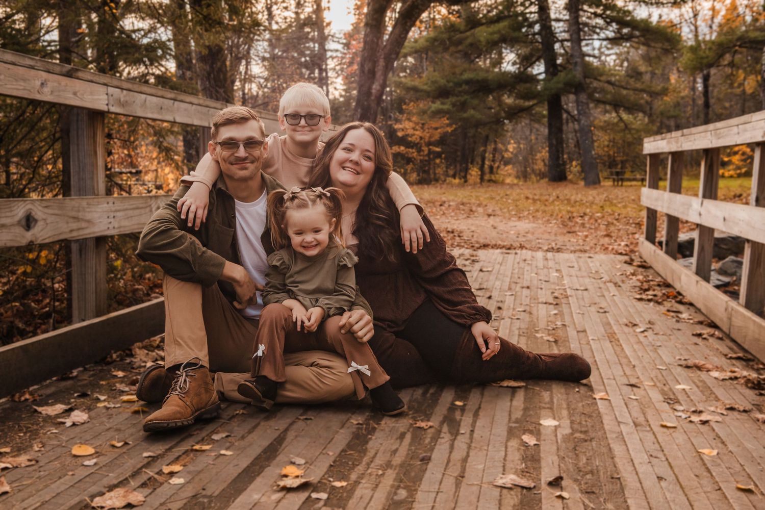 A family sits together on wooden steps during a fall photo session in a forest setting.