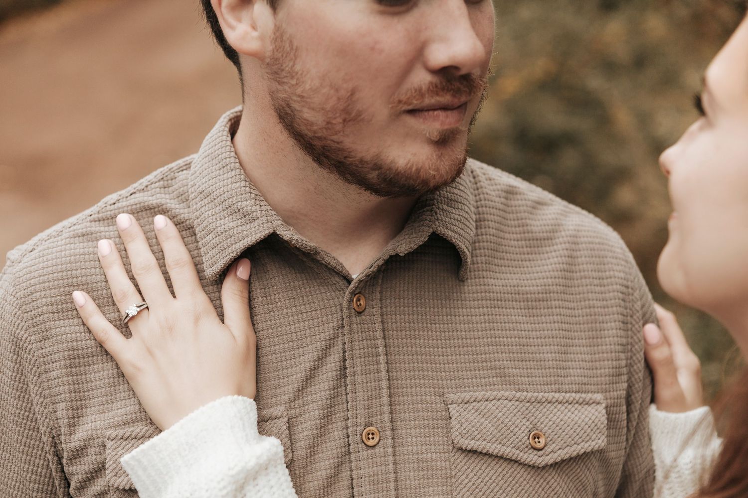 Close up of a couple sharing an intimate moment outdoors, with a hand resting on a brown corduroy shirt.