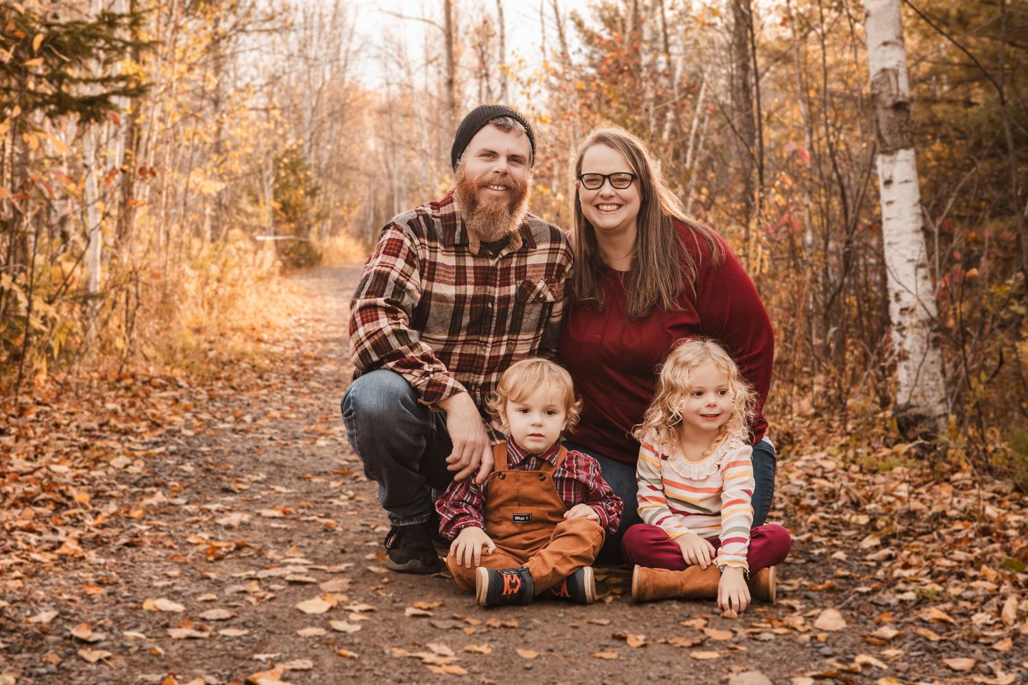 Family enjoying a fall day together on a path covered in golden autumn leaves.