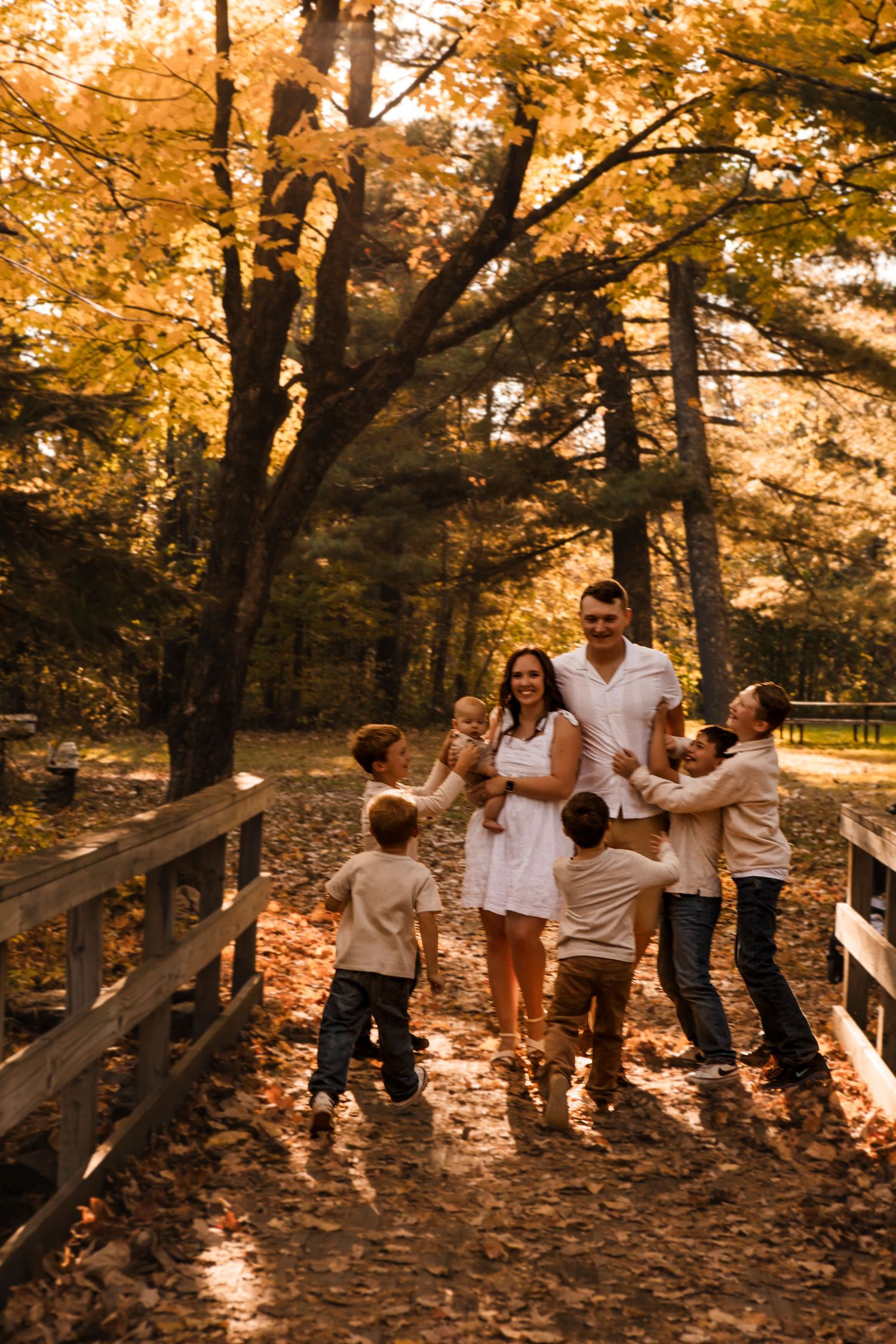 A family plays together on a wooden bridge surrounded by golden autumn trees during sunset.