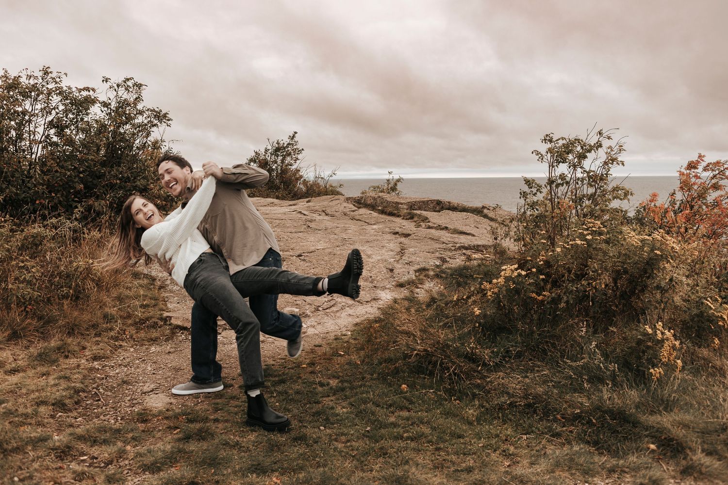 A couple poses together in a rustic outdoor setting during golden hour on a hillside with autumn foliage.