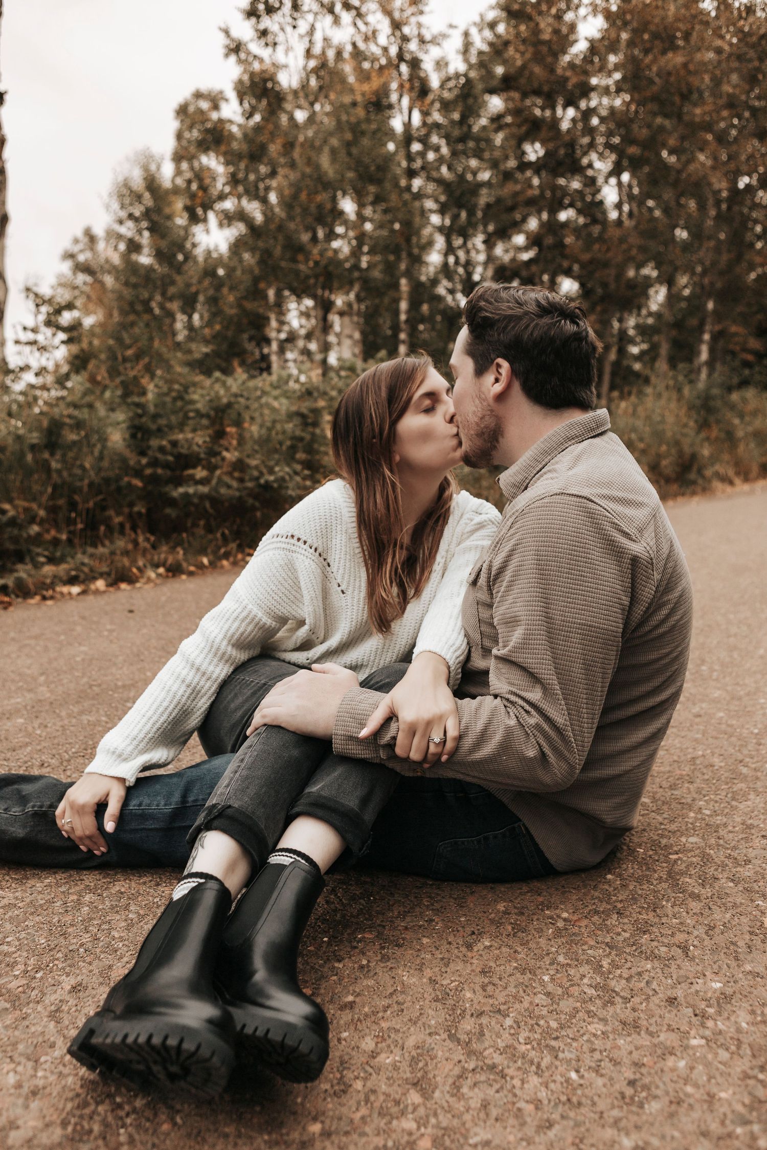 A couple shares tender moments lying on autumn ground wearing cozy sweaters in a romantic outdoor photoshoot series.