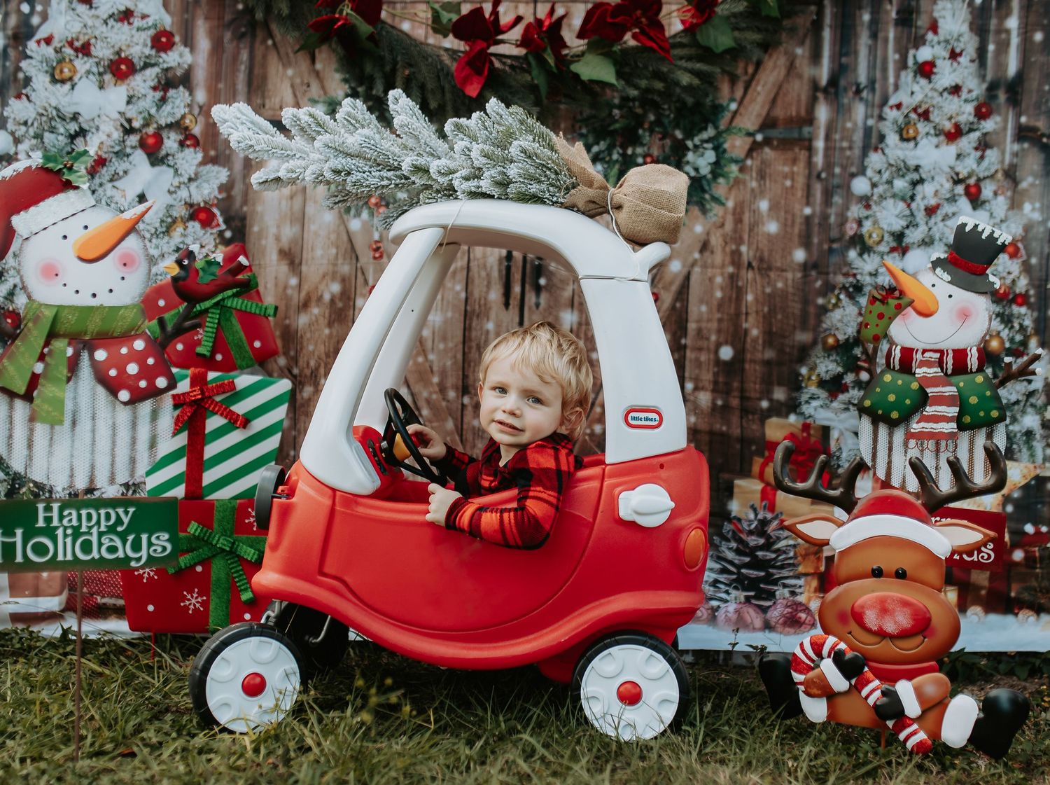 Festive holiday scene with a red toy cozy coupe car surrounded by snowman and Christmas decorations against a wooden backdrop.