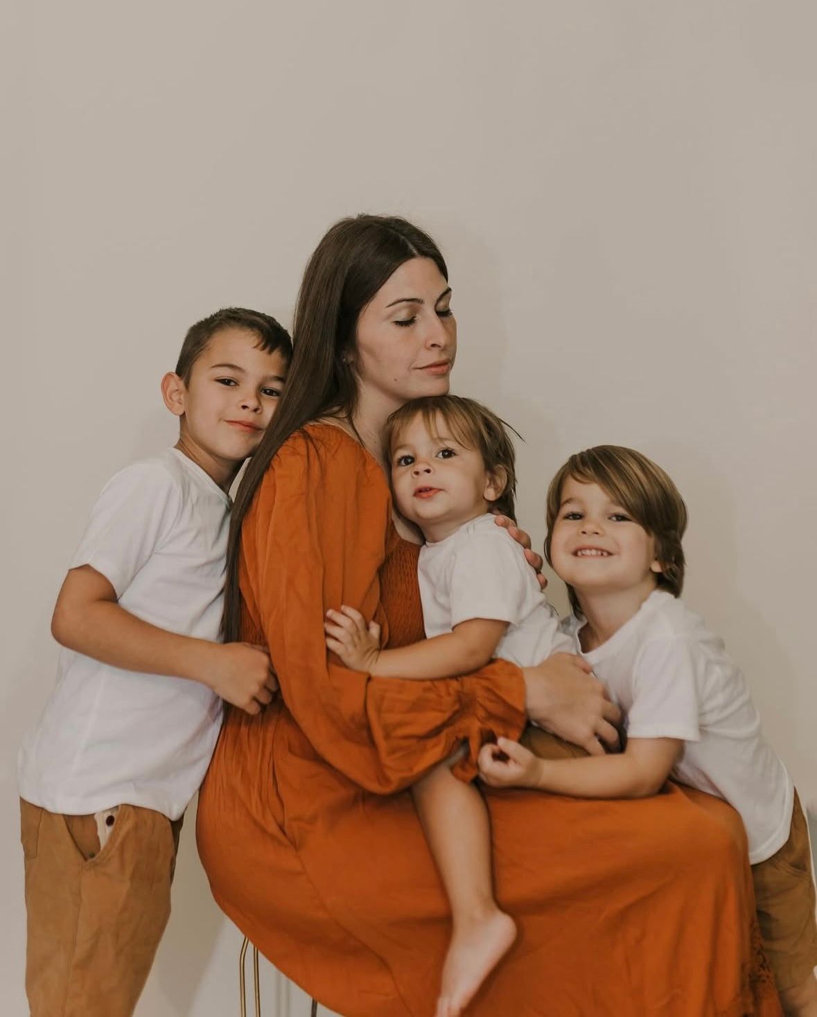 A family in coordinated white and orange outfits poses together against a neutral background for a warm portrait.