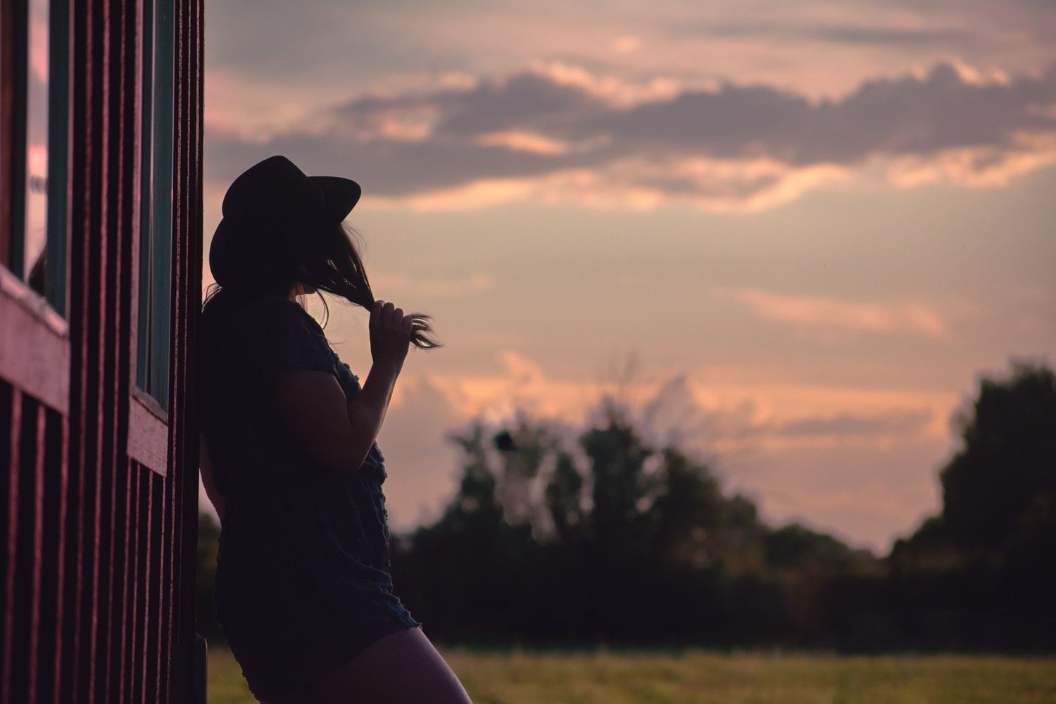 Sunset landscape with female leaning against a barn silhouetted by the sky