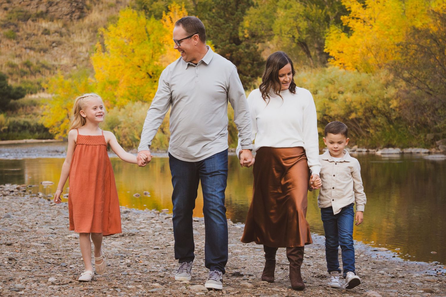 Family of four walking hand in hand by the river during the fall