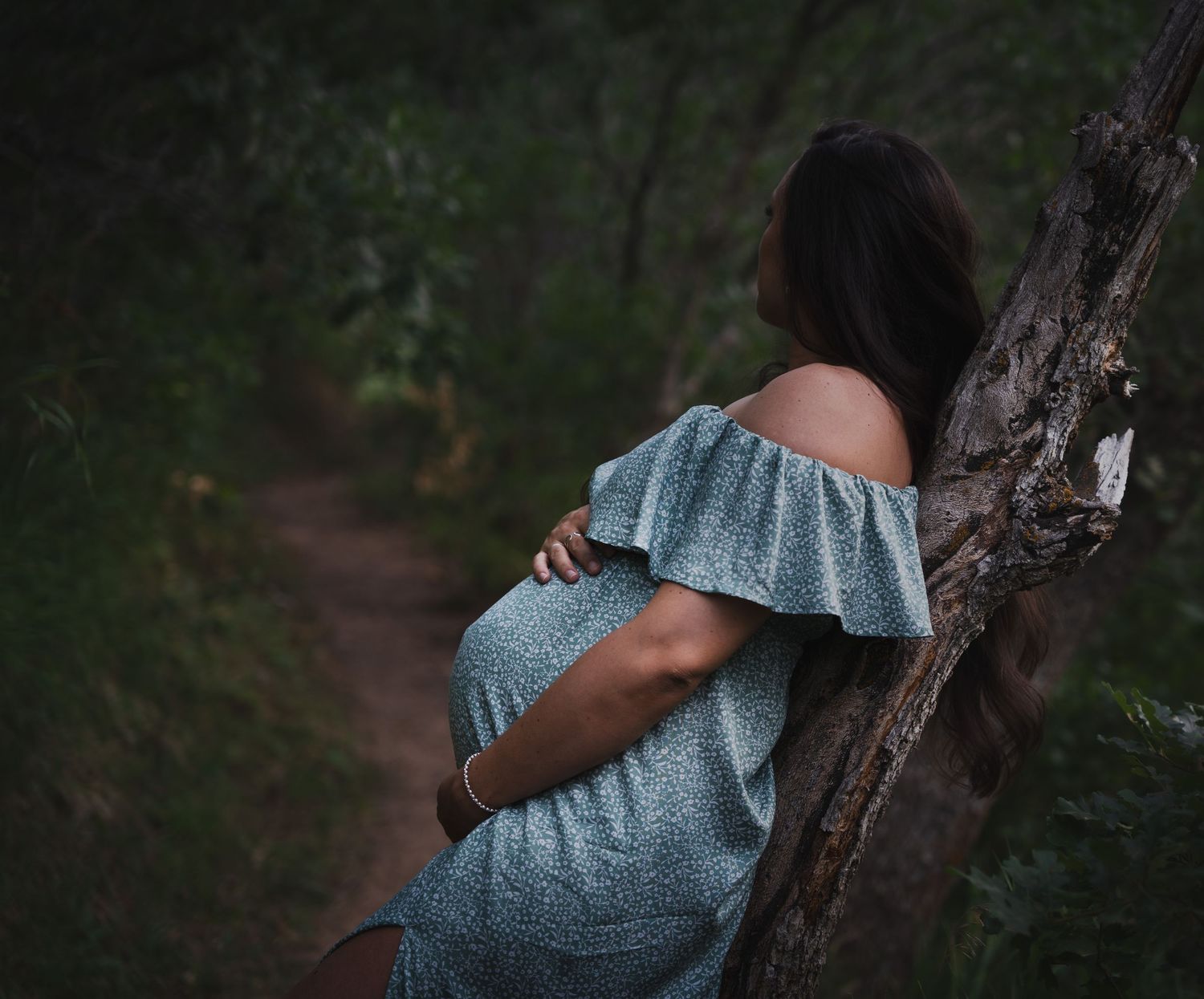 Woman looking into the distance holding her pregnant belly in the forest