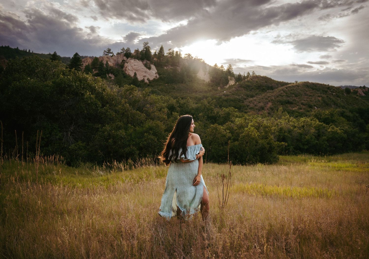 Woman in a dress standing in a field at sunset looking into the distance