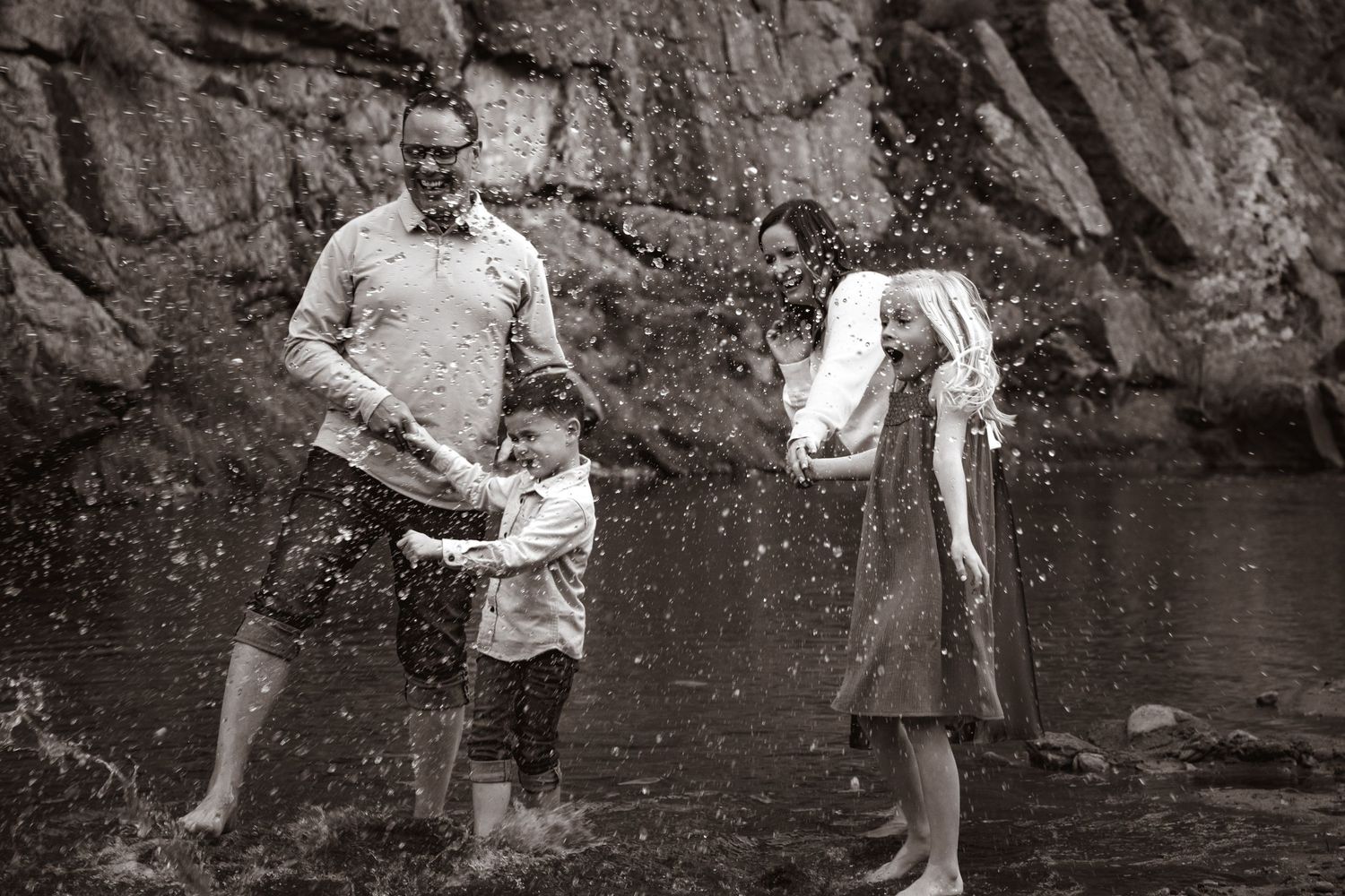 Family of four playing in a river kicking water in the air