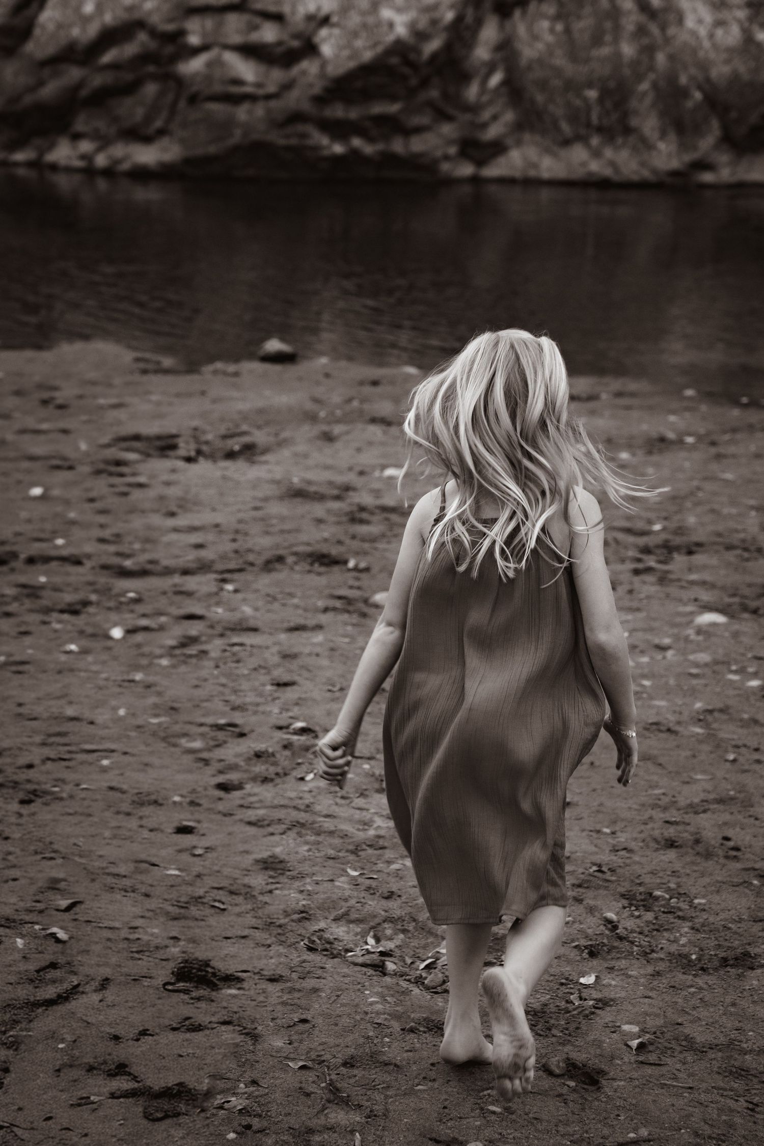 Black and white photo of a girl in a dress running towards the river